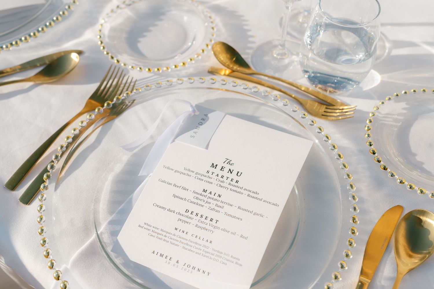 Wedding place settings with gold cutlery and menu cards decorated with pearl beading.