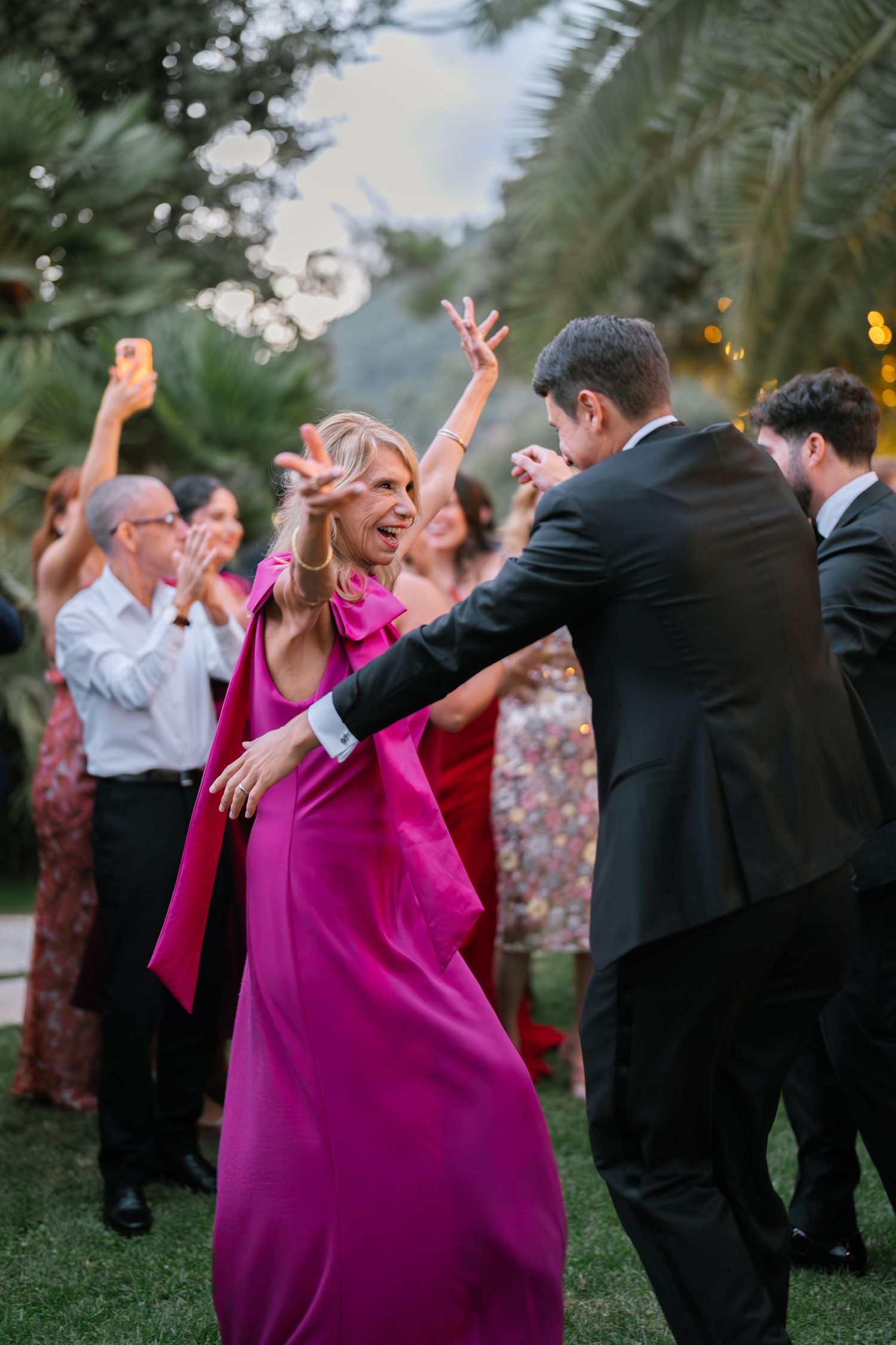 Wedding guests dancing and celebrating with joyful energy in bright fuchsia and black formal attire.