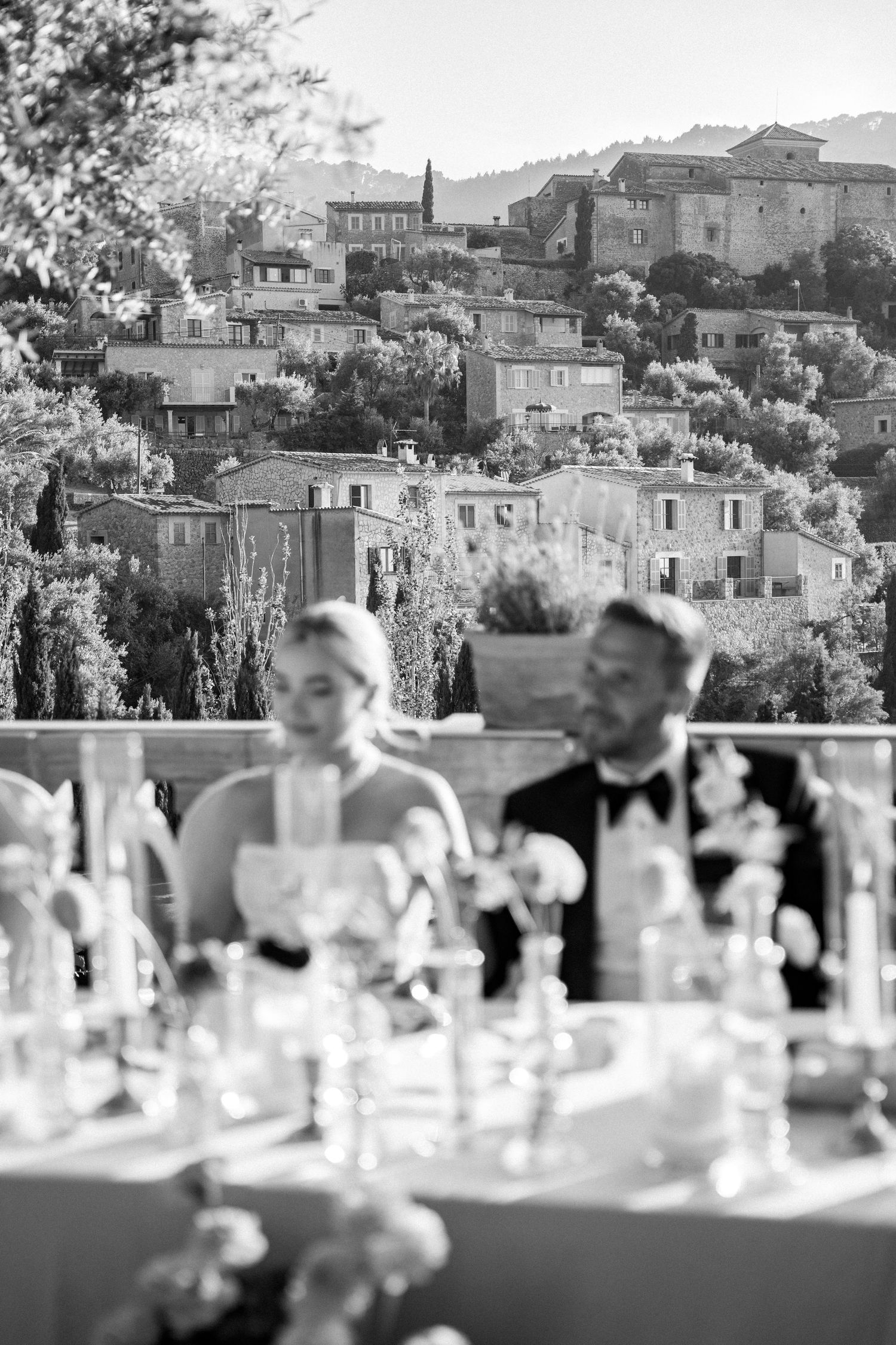 Wedding reception tables set against a scenic Mediterranean hillside village backdrop.
