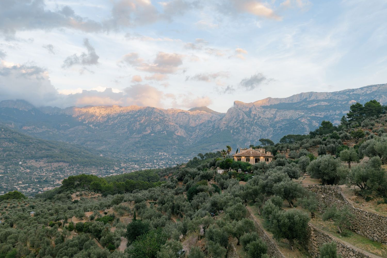 Scenic panoramic view of a Mediterranean coastal mountain landscape with scattered villas and lush greenery at sunset.