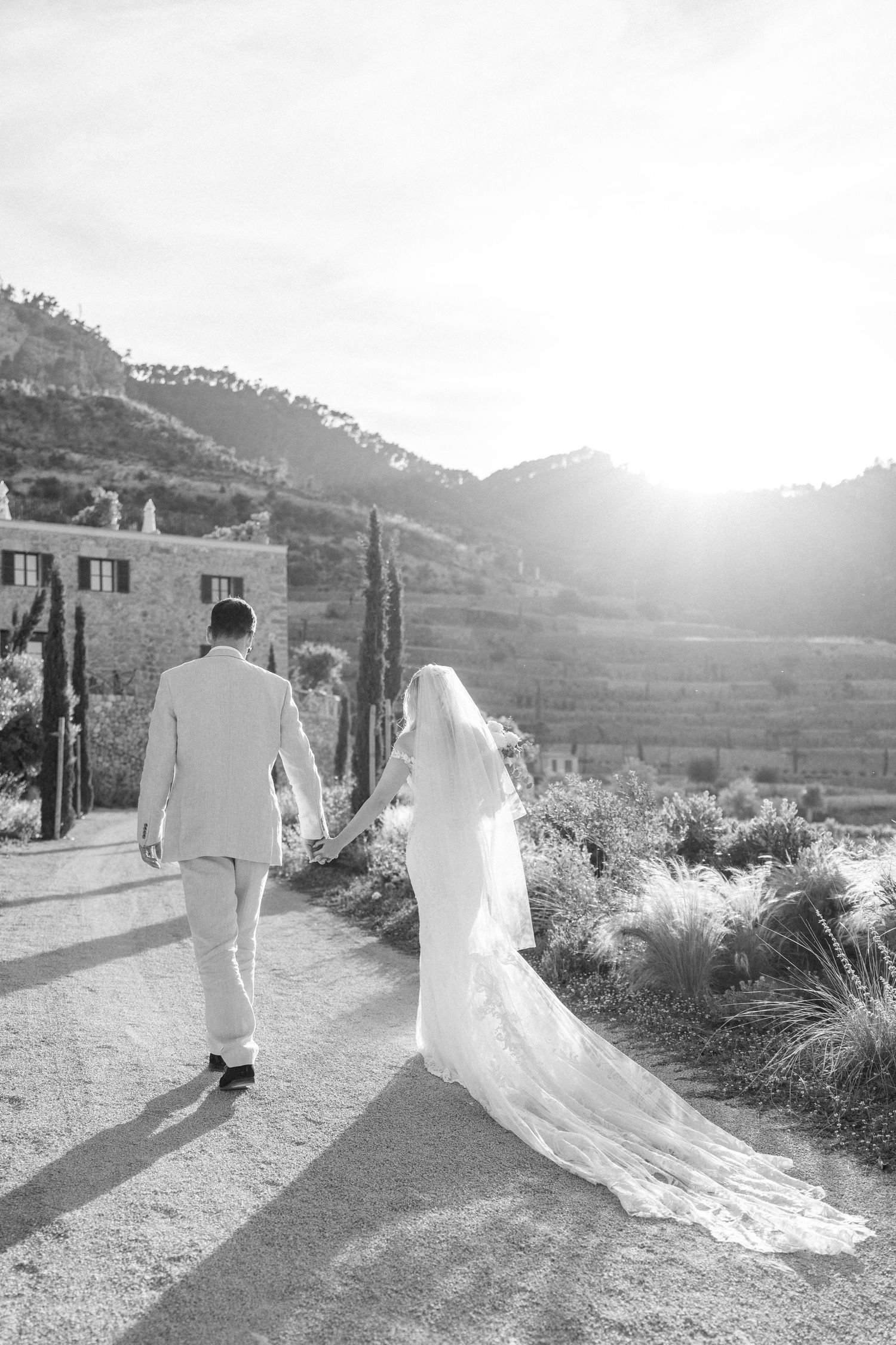 Wedding couple strolling along a scenic mountain path with trailing white dress and veil.
