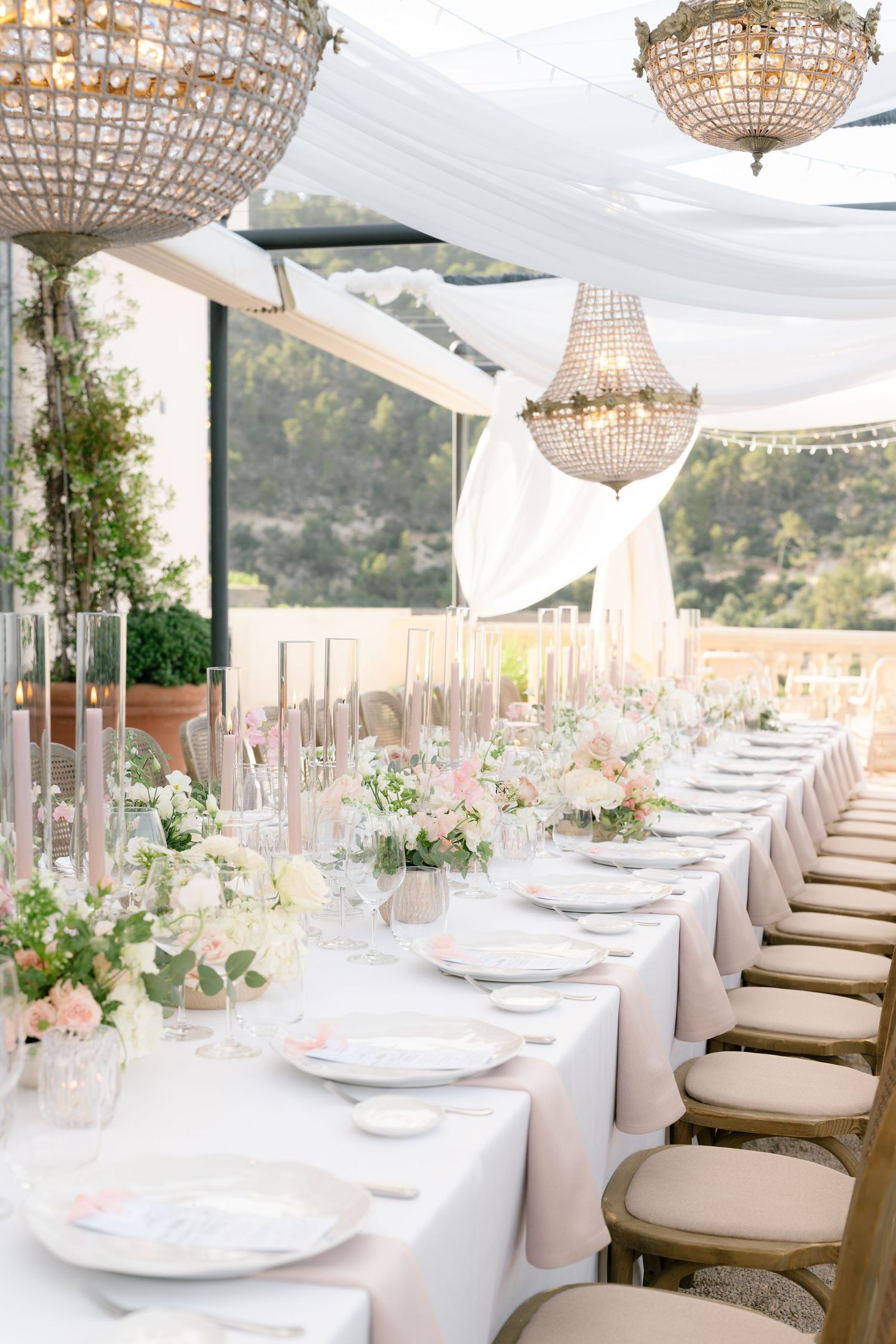 Luxurious outdoor reception setup with crystal chandeliers and white table settings.