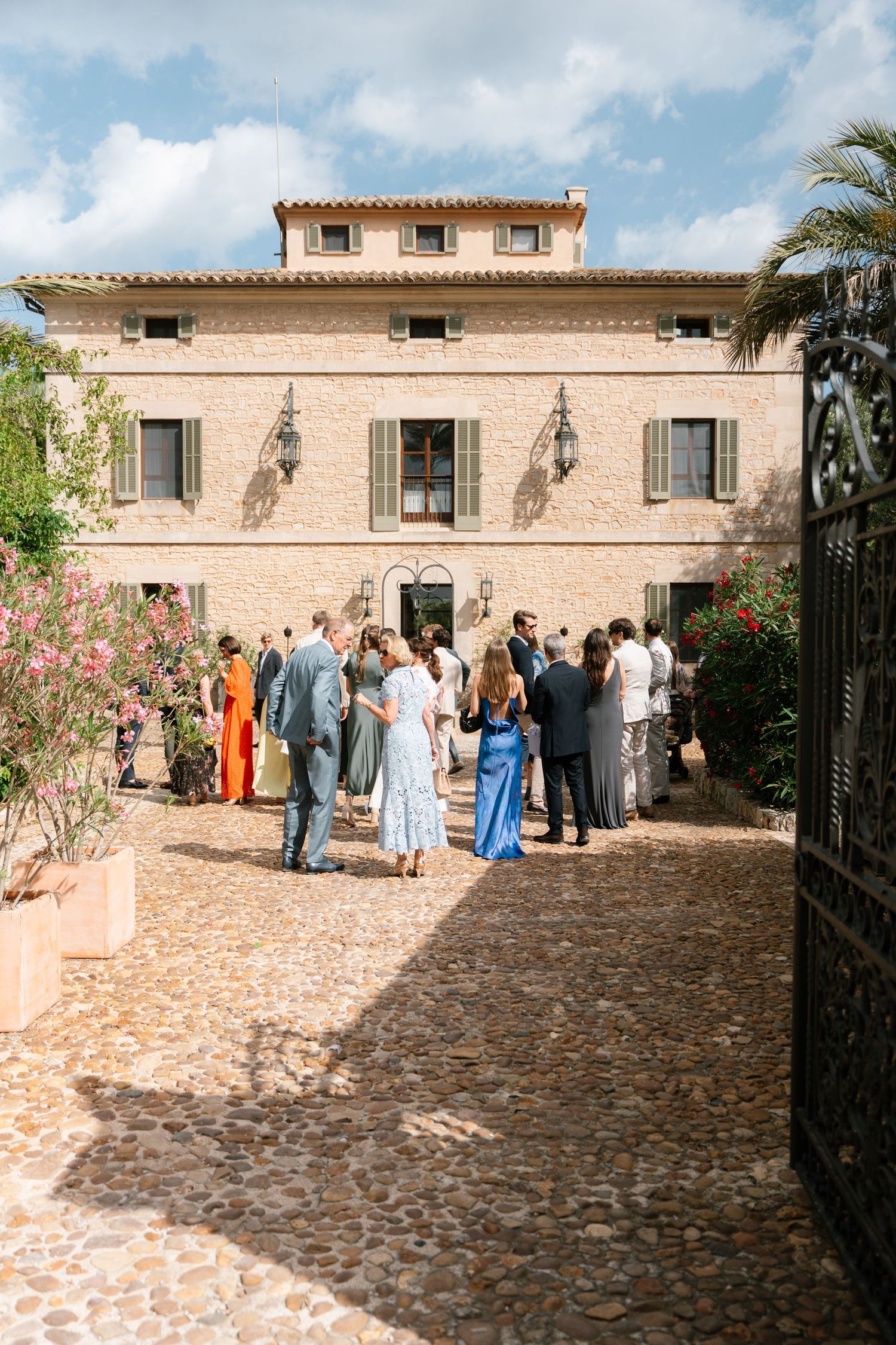 Elegant stone courtyard with palm trees hosts formally dressed wedding guests during a daytime reception.