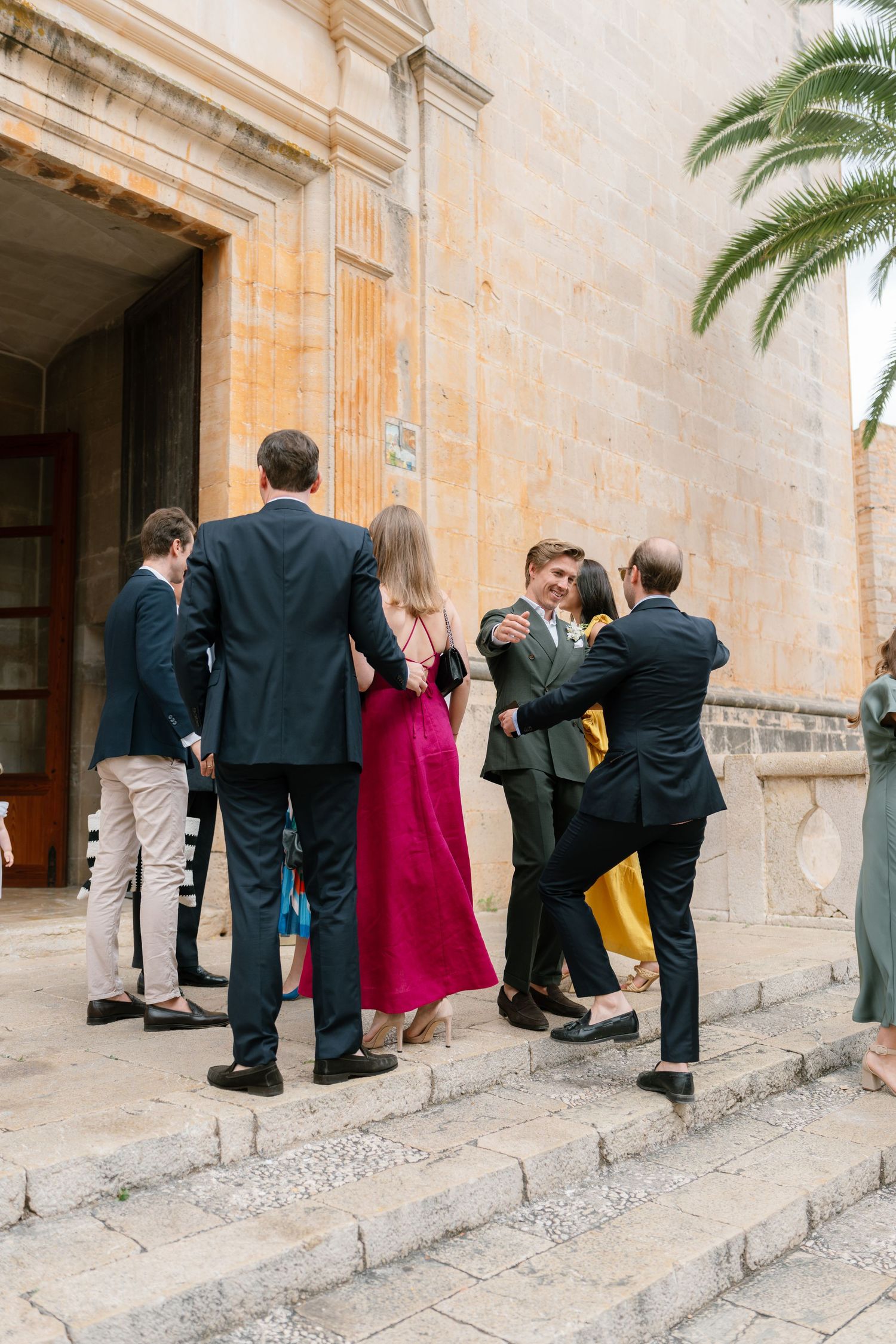 Wedding guests ascending stone steps of a historic Mediterranean church.