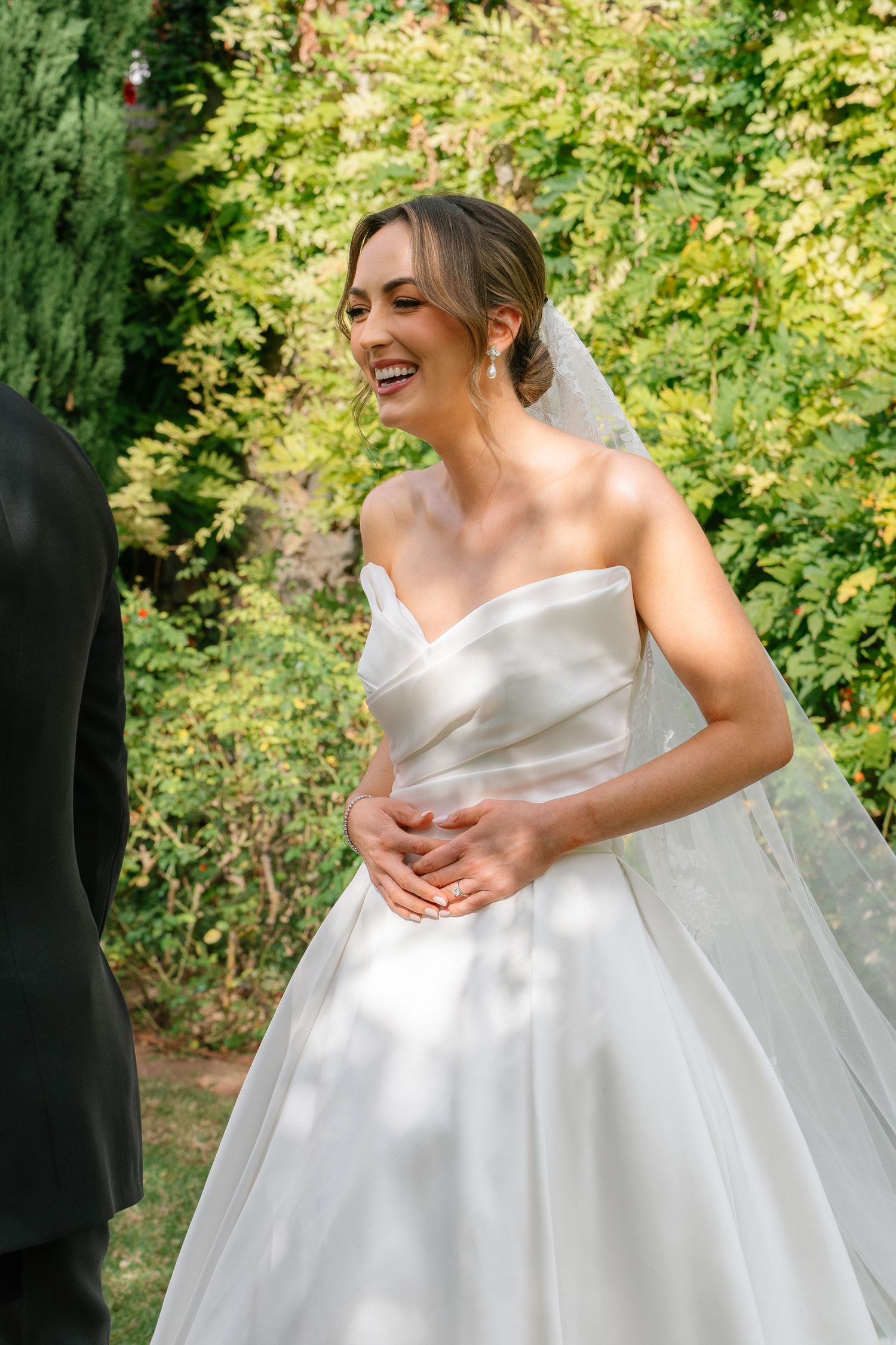Bride in flowing white ballgown adjusting dress in garden setting.