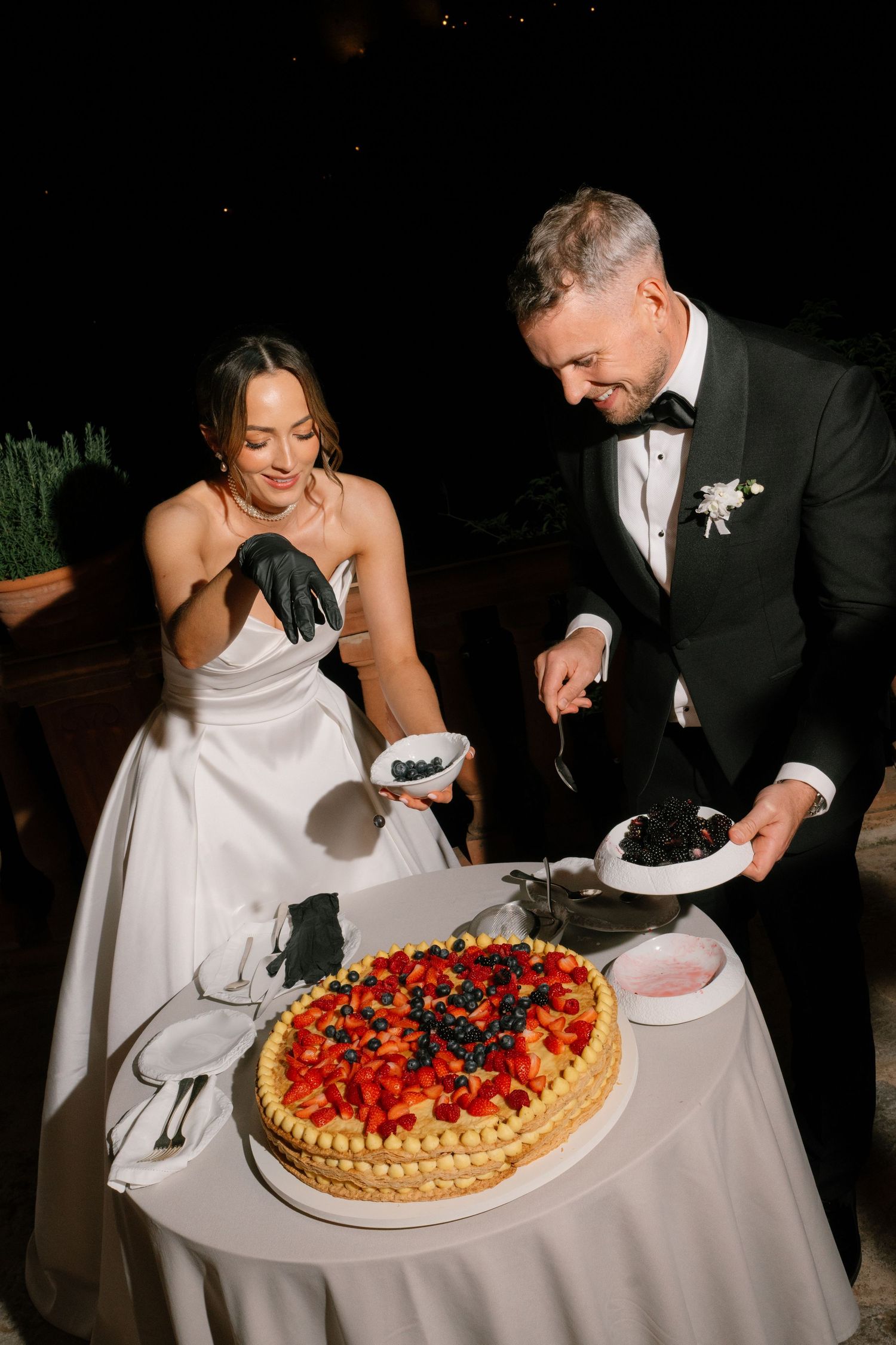 Couple cutting into a beautiful fruit-topped wedding cake at their evening reception.
