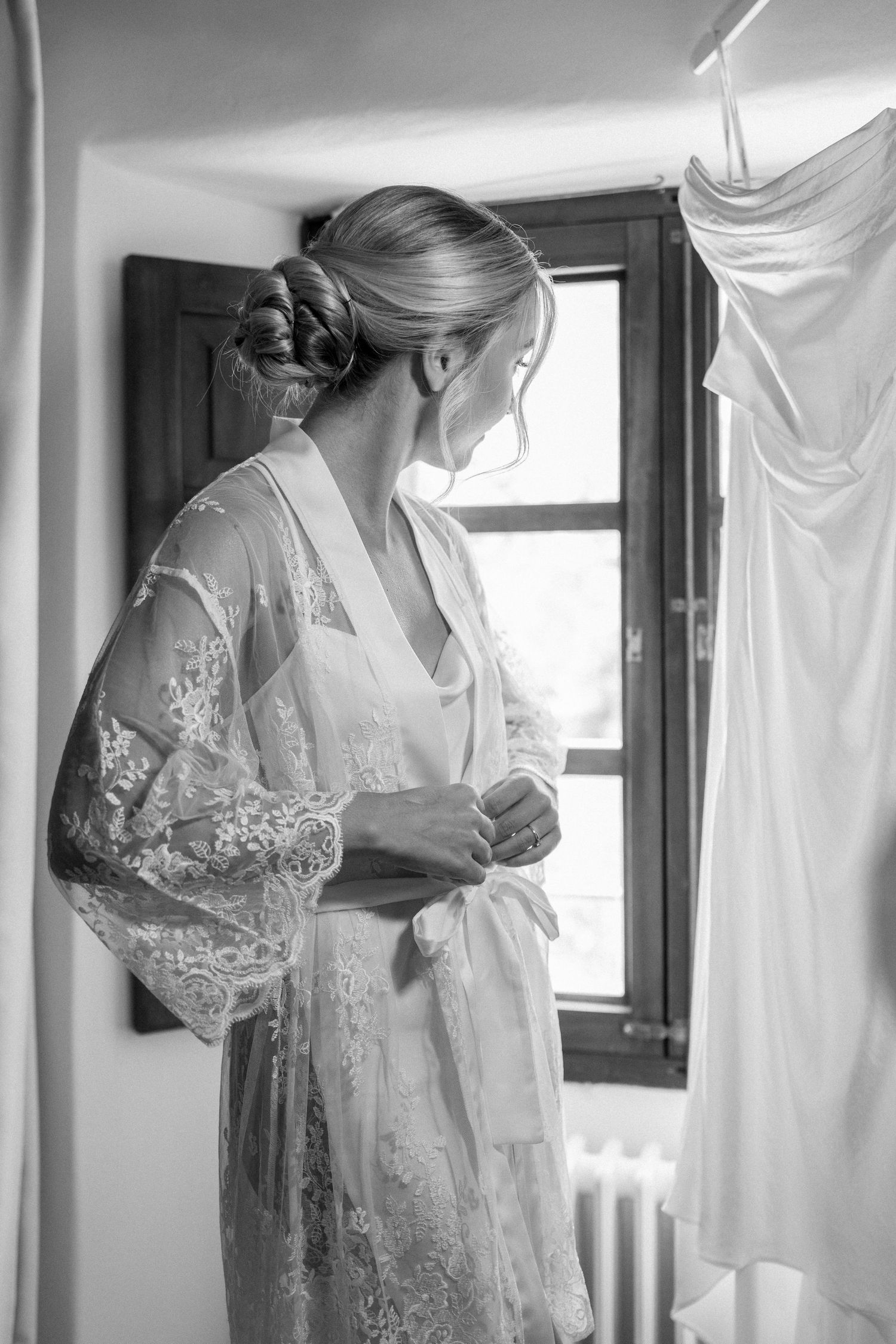 Delicate white wedding dresses and robes hanging in a sunlit room with lace details.
