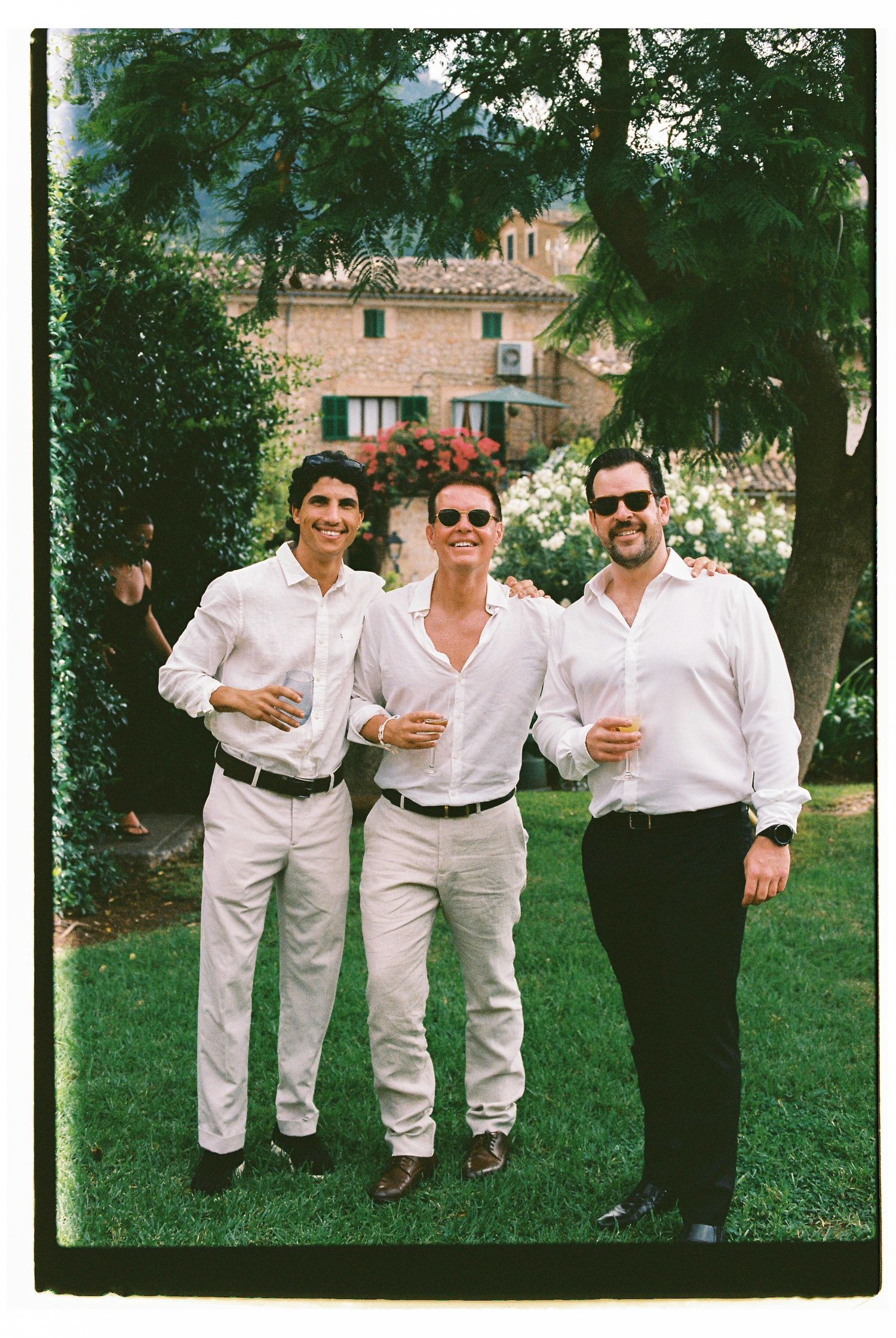 Three guests in white shirts enjoying drinks at an outdoor wedding reception.