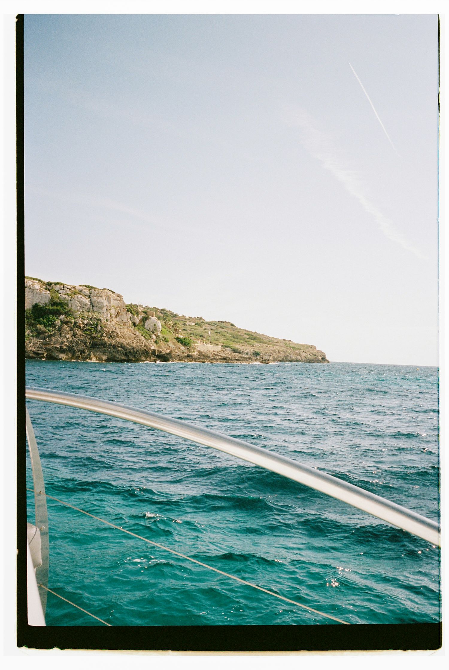 Rocky coastline and turquoise waters viewed from a boat with railing in foreground.