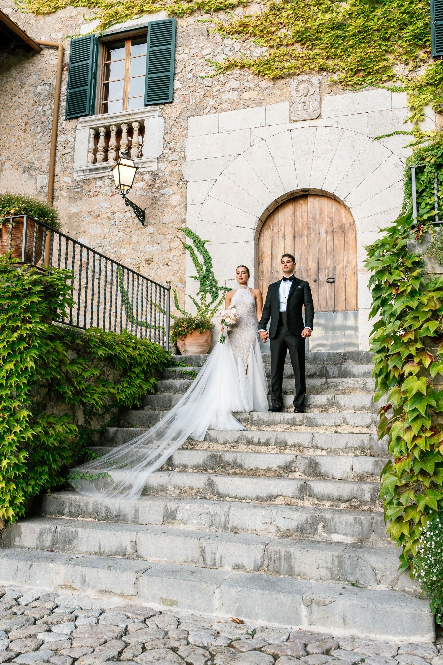 Wedding couple ascending stone steps at rustic venue with ivy-covered walls.
