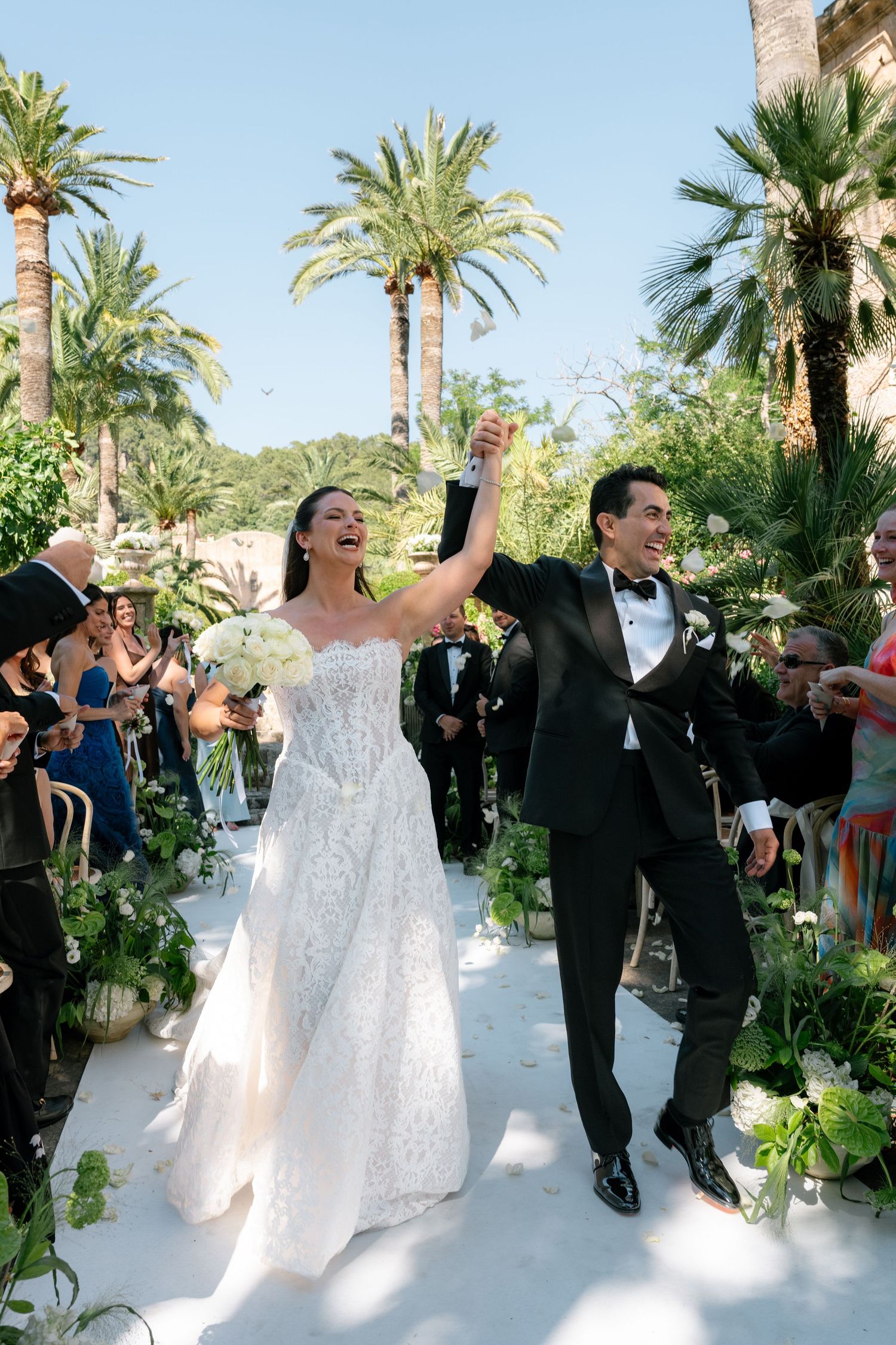 Joyful newlyweds celebrate recessional at outdoor wedding ceremony surrounded by palm trees and lush greenery.