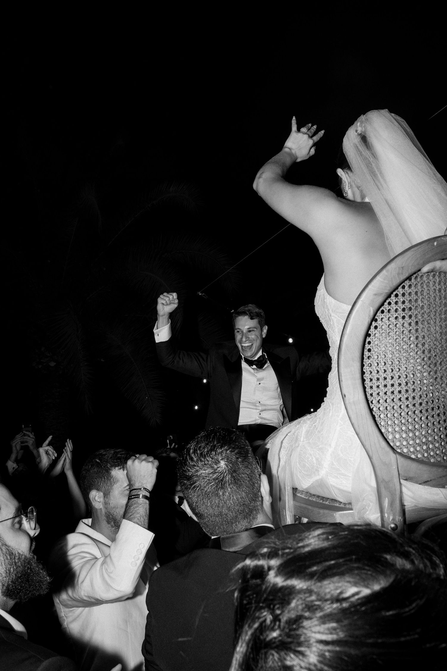Black and white photo of lively dancing and celebration at a nighttime wedding reception.