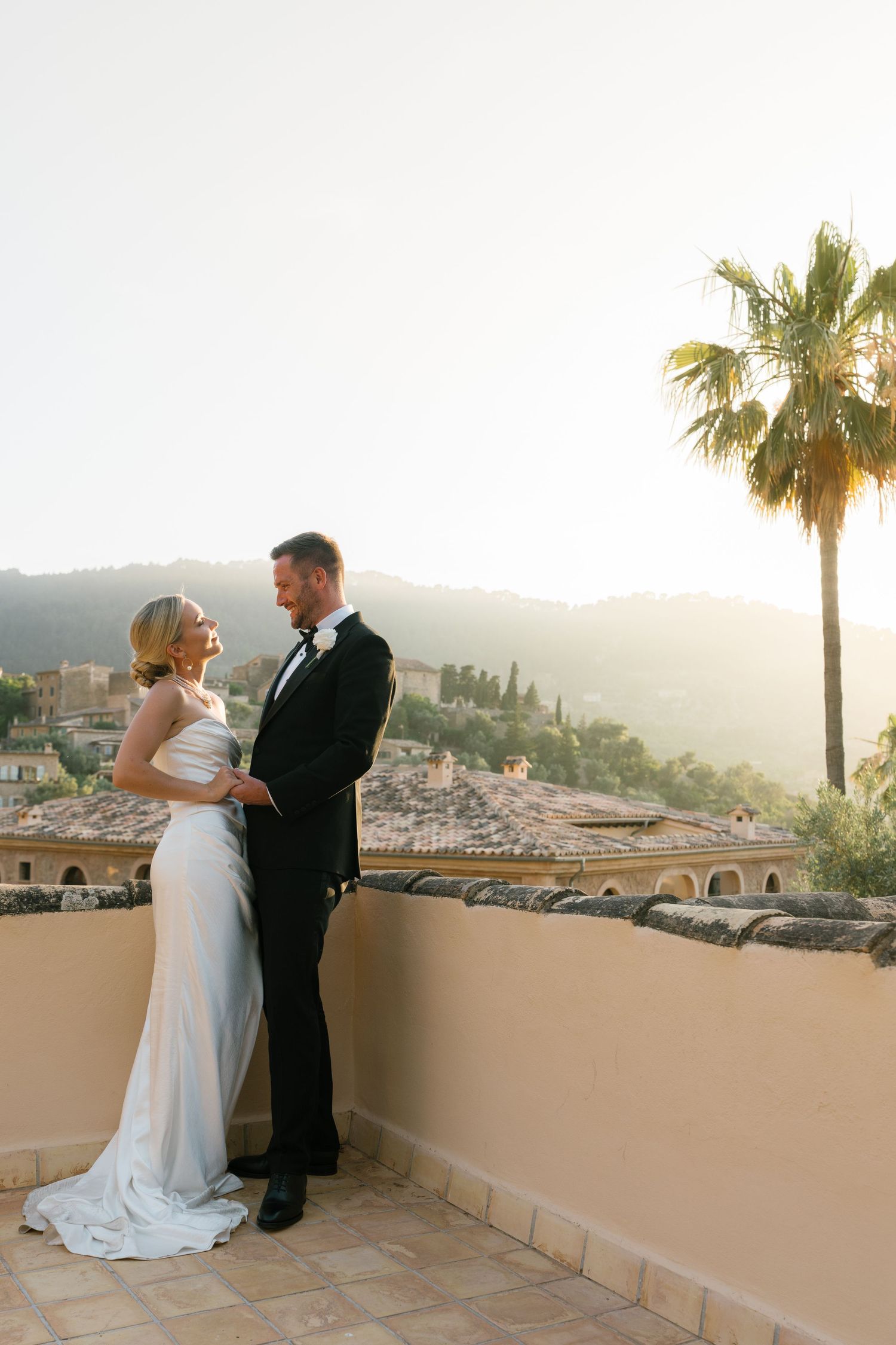 Sunset wedding portraits on a Mediterranean terrace with palm trees and mountain views.