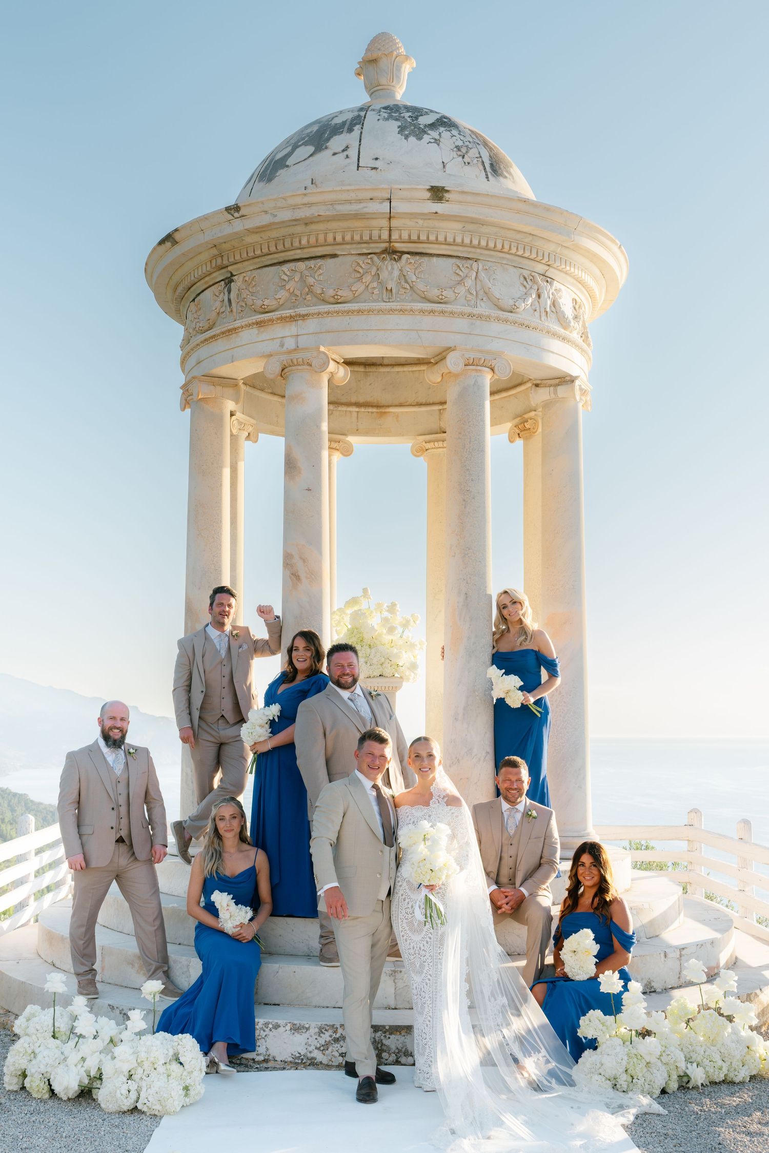 Wedding party posing in a white stone gazebo decorated with flowers.