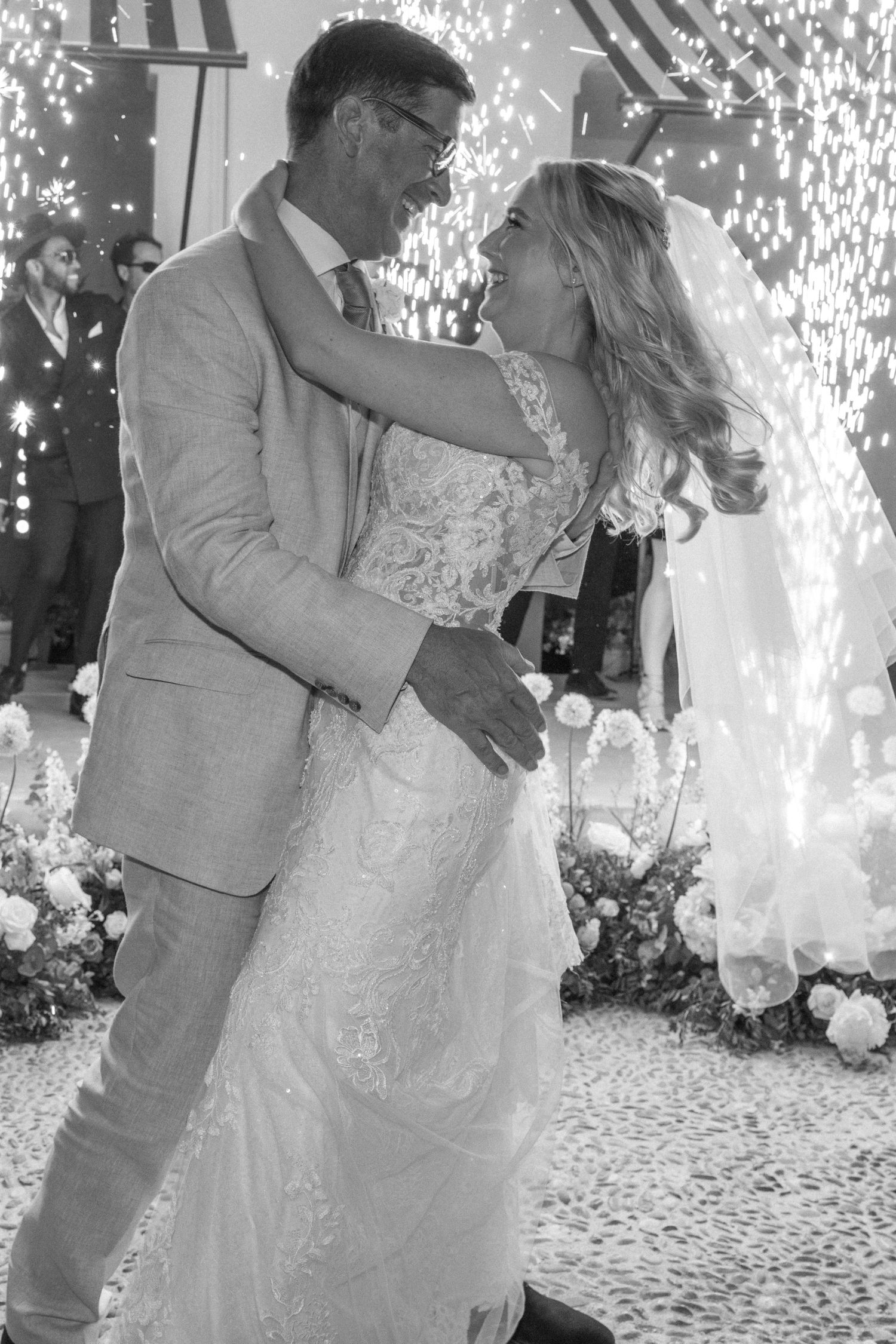 Couple sharing first dance at wedding reception with sparkler effects in background.