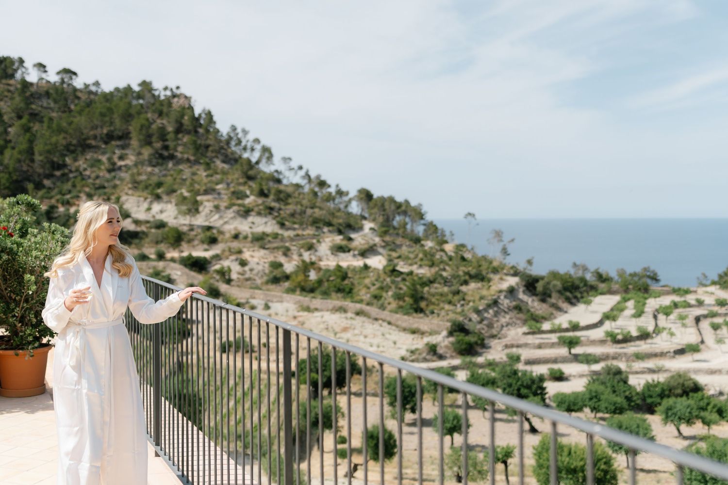 Woman in white dress admires stunning coastal mountain view from balcony.