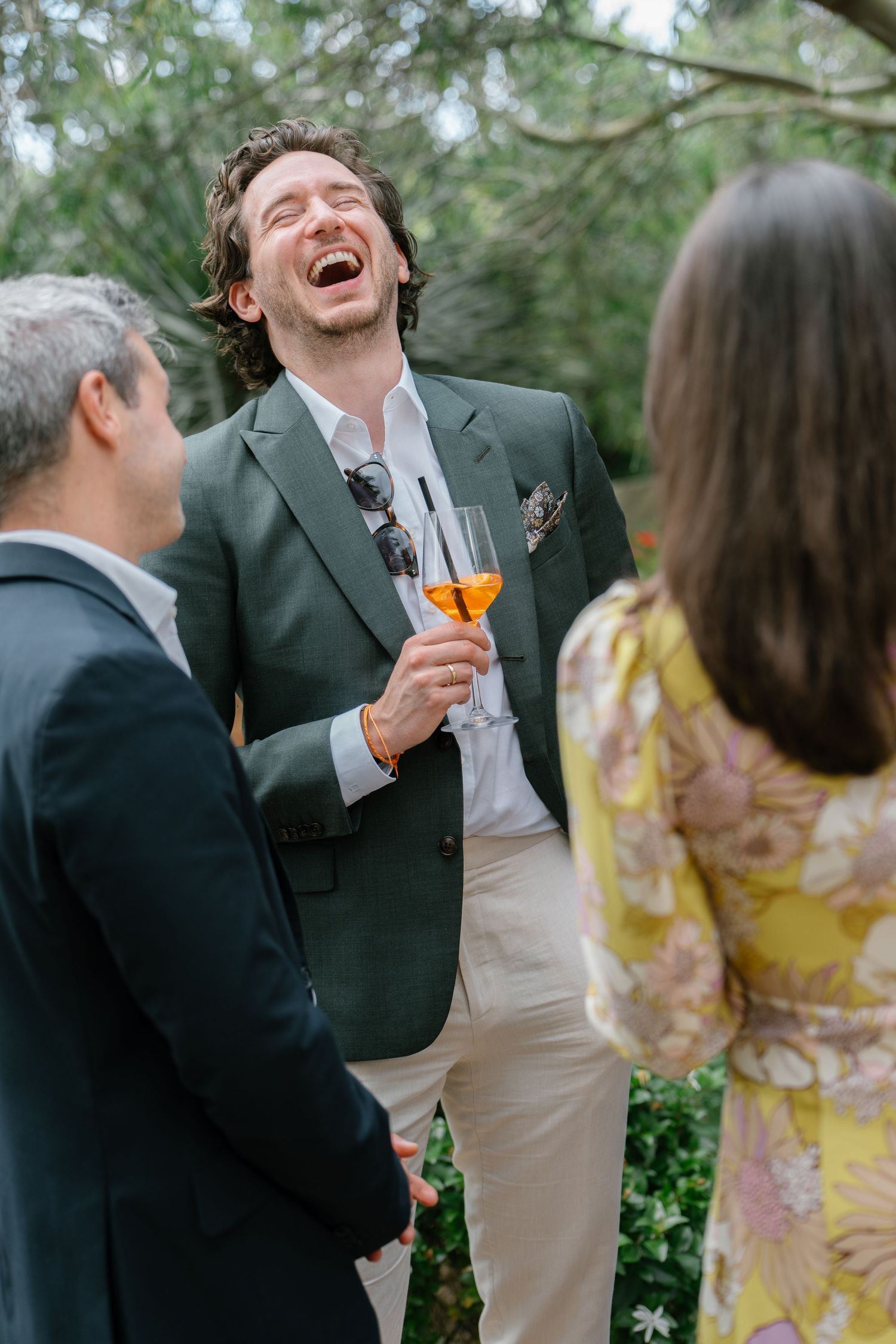 Wedding guests share laughter and conversation during an outdoor cocktail reception.