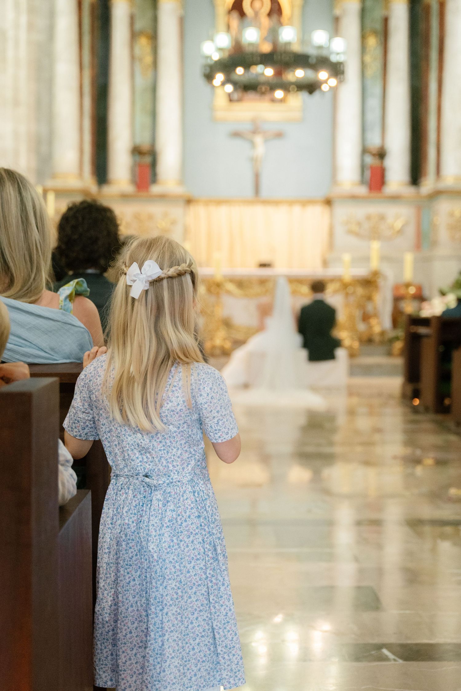 Young attendant in a light blue floral dress walking through an ornate church interior.