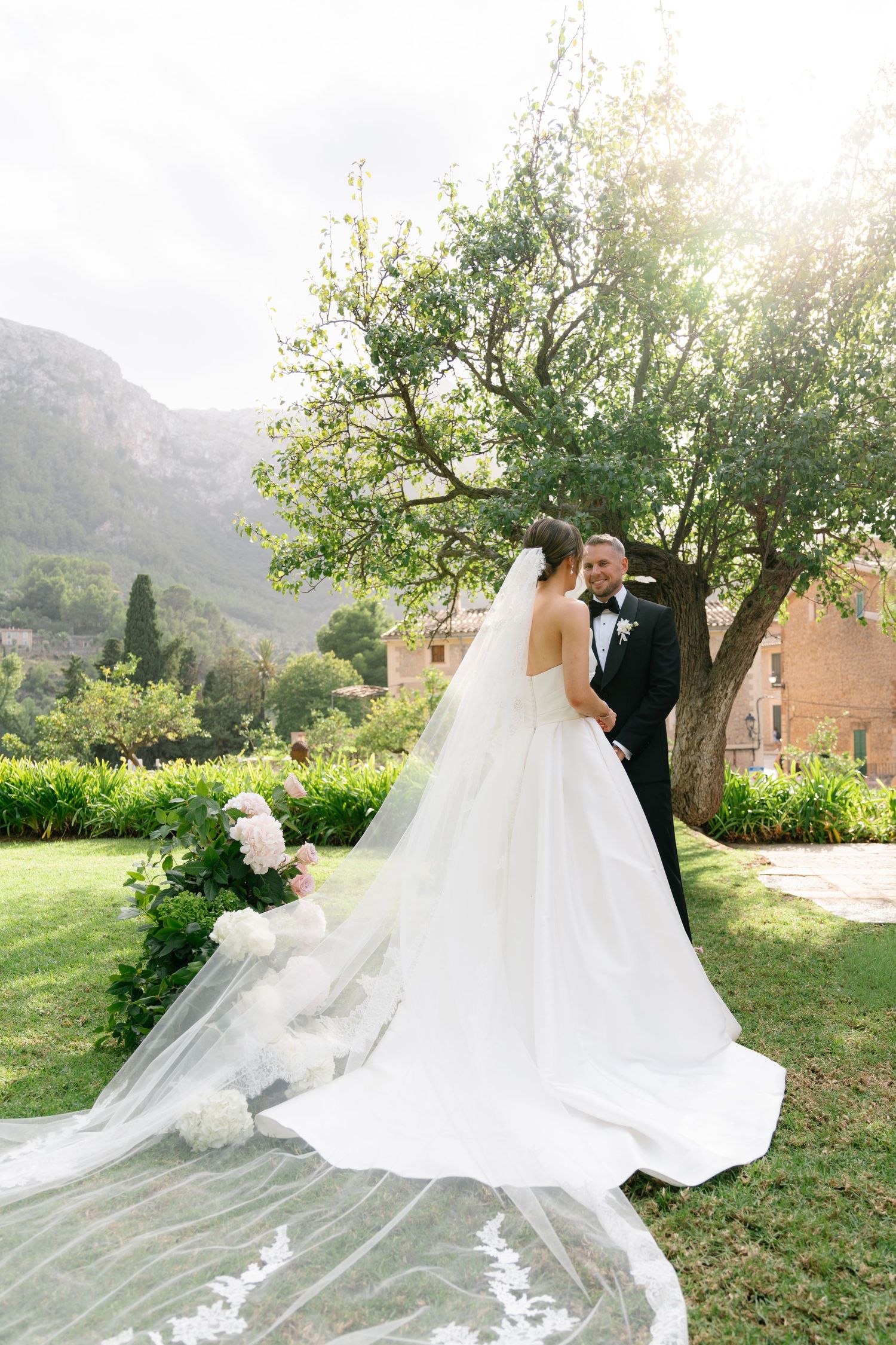 A dramatic wedding dress train flows across lush green grass with mountains in the background.