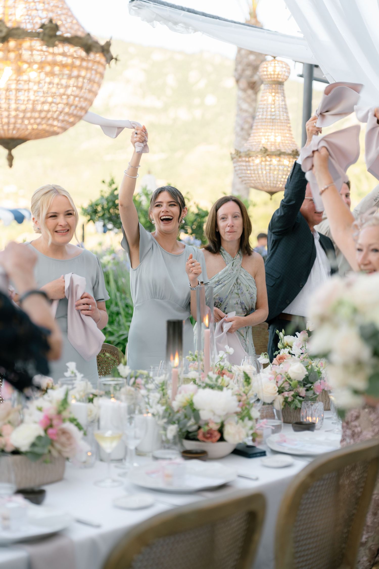 Wedding reception table with guests celebrating and raising their hands in joy.