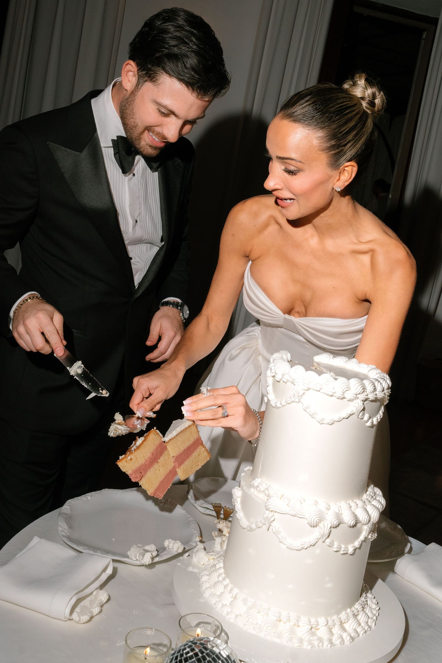 A couple cuts into their elegant white tiered wedding cake together at their reception.
