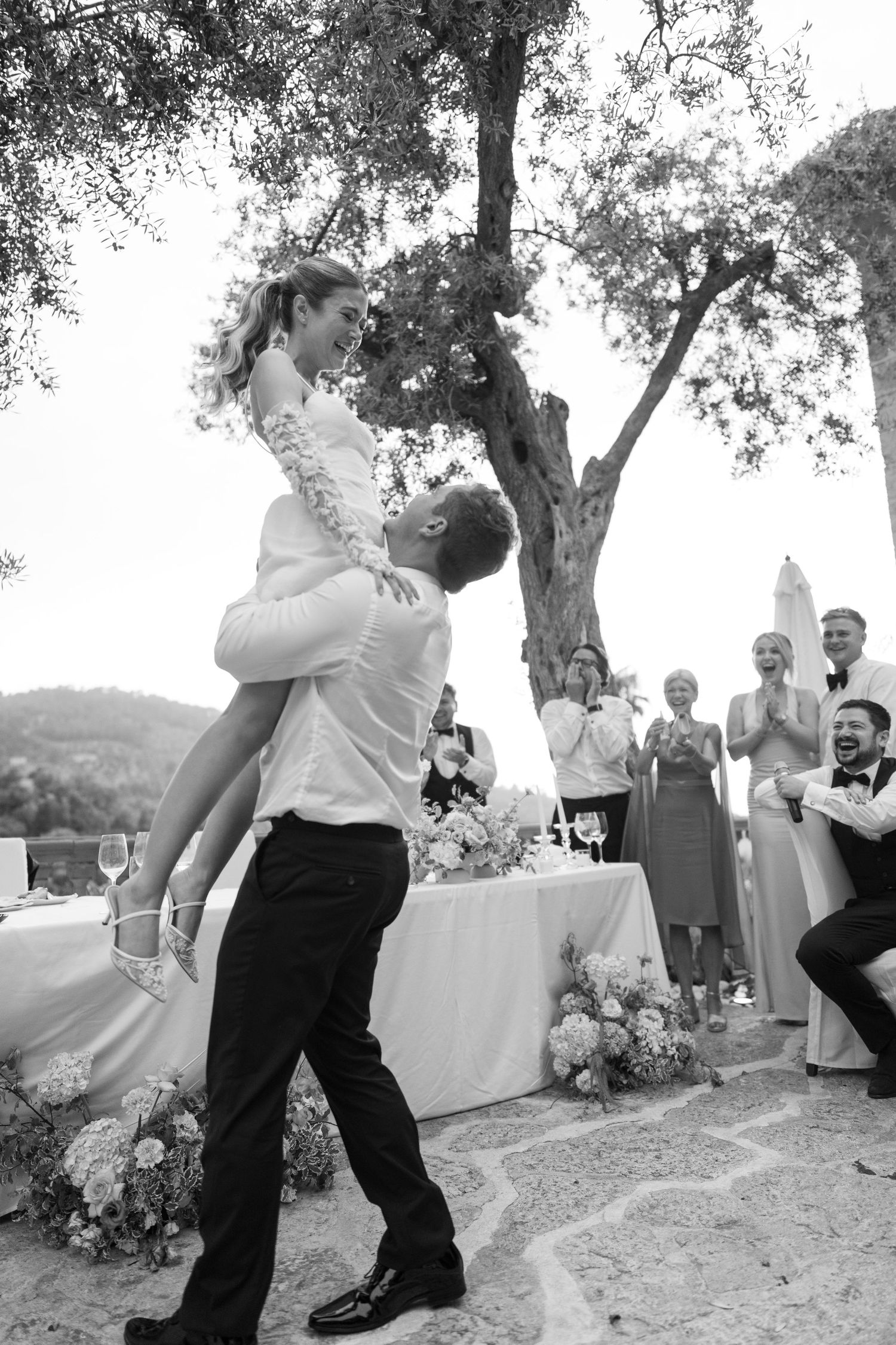 Black and white wedding dance sequence showing joyful celebration under trees.