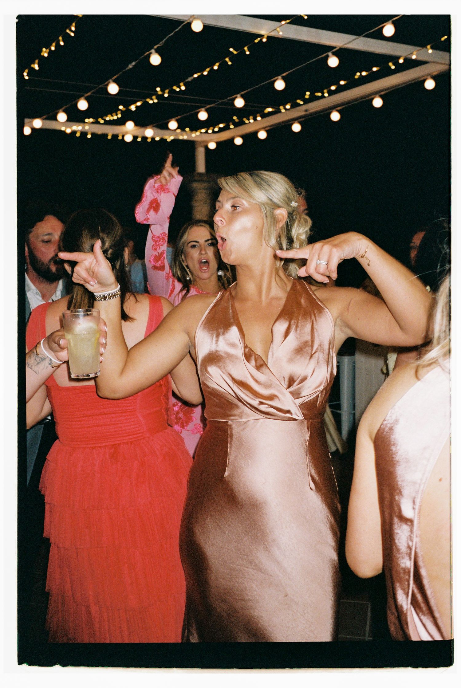 People dancing under string lights at an evening celebration.