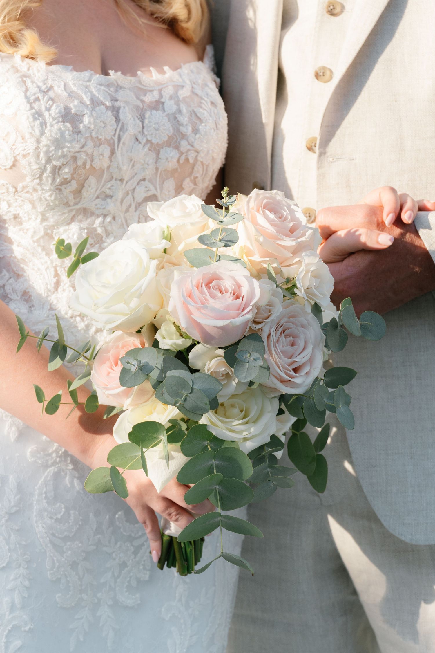 Close-up of delicate pink and white rose bouquet with eucalyptus leaves against lace dress.