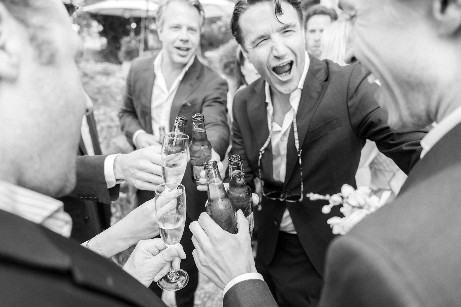 Black and white photo captures joyful laughter among guests at a wedding reception.