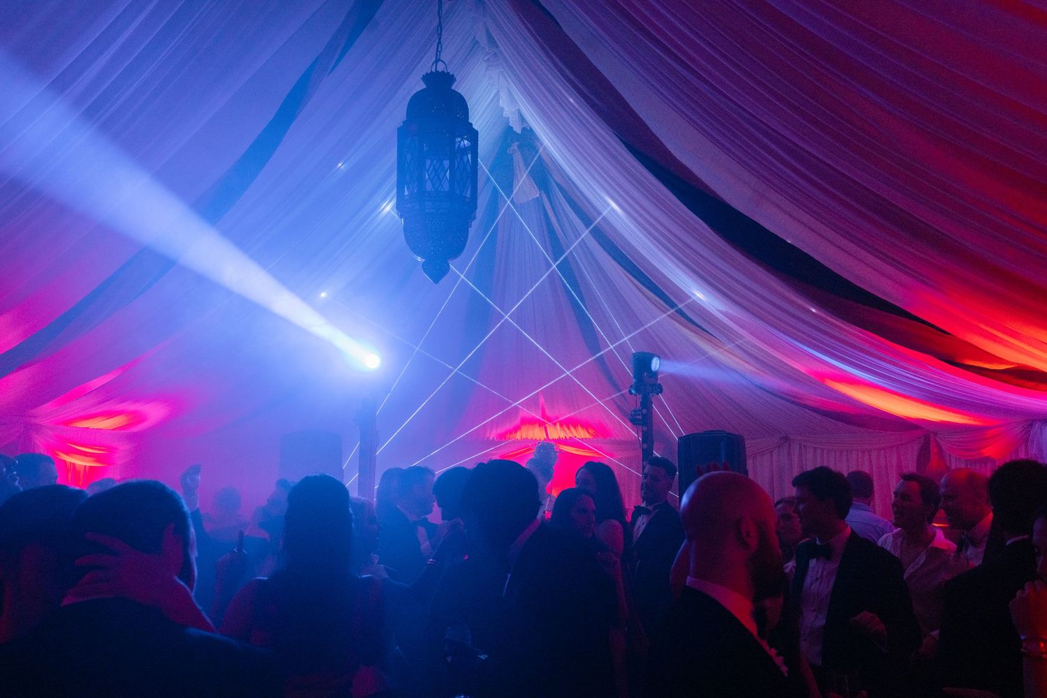 Colorful lighting illuminates tent ceiling during evening wedding reception.