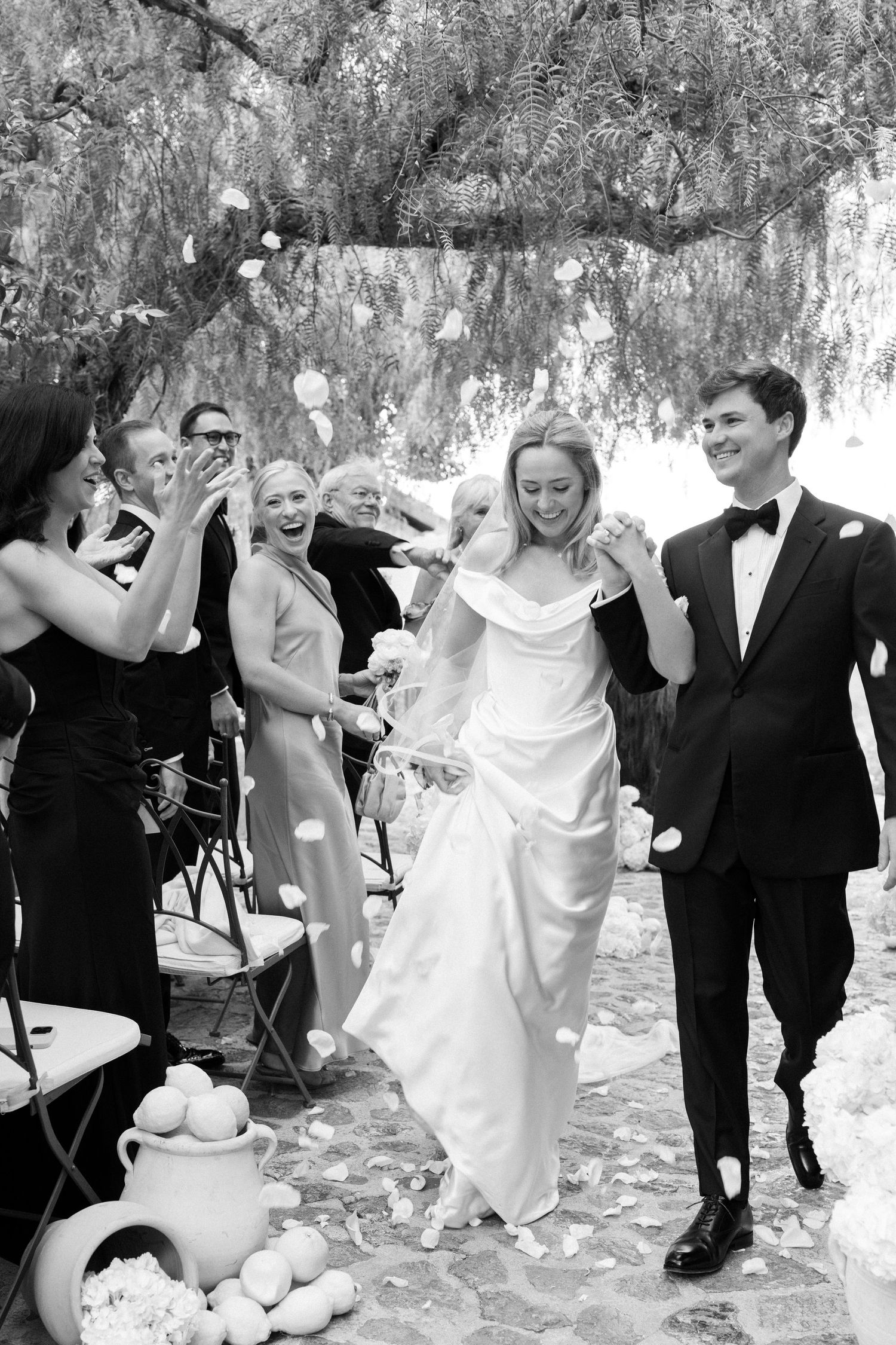Wedding party celebrates outdoors under weeping willow trees during daytime festivities.