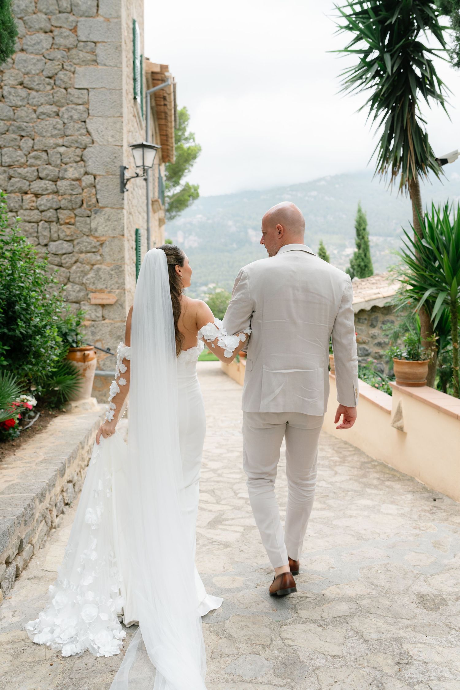 Wedding couple walking along stone pathway with mountain views and tropical plants.