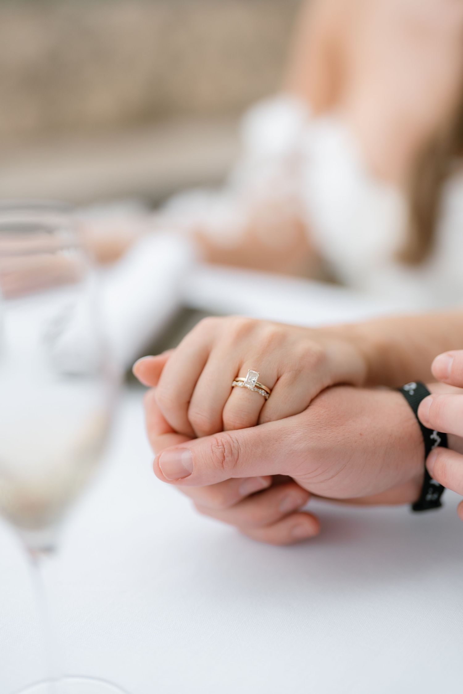 Close-up of hands with wedding rings resting on a white surface.