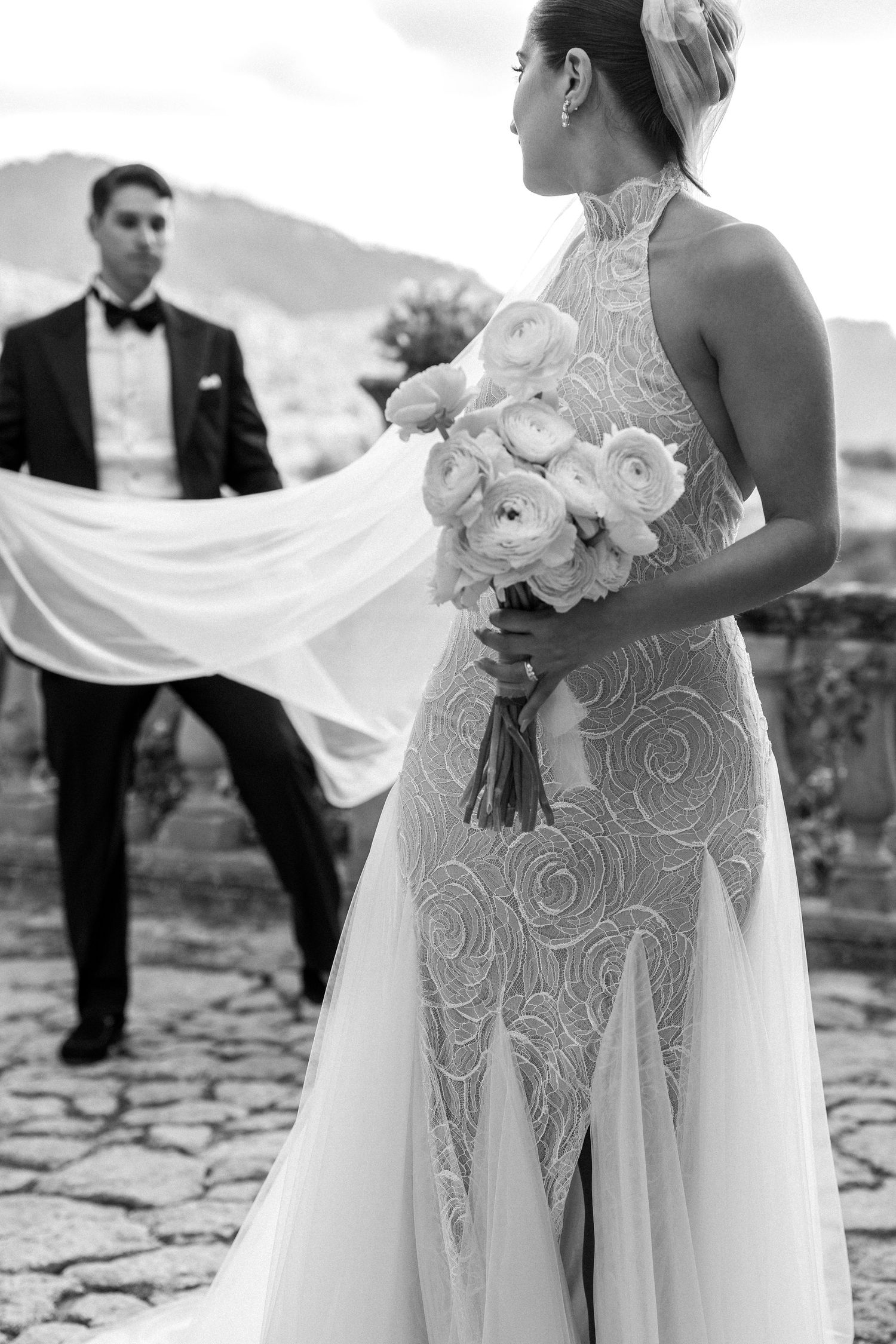 Black and white photo showing details of a lace wedding dress and bouquet.