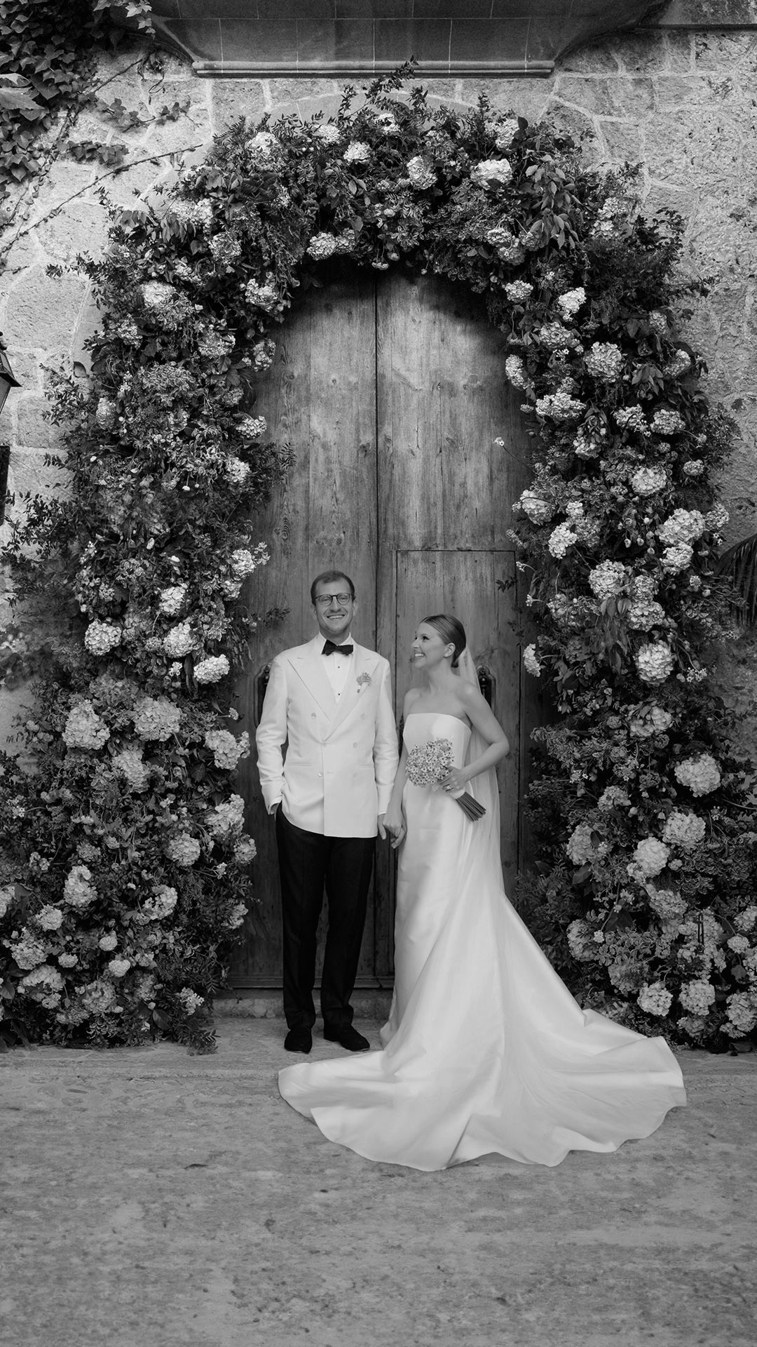 Formal wedding portraits taken against a backdrop of climbing roses and rustic wooden doors.