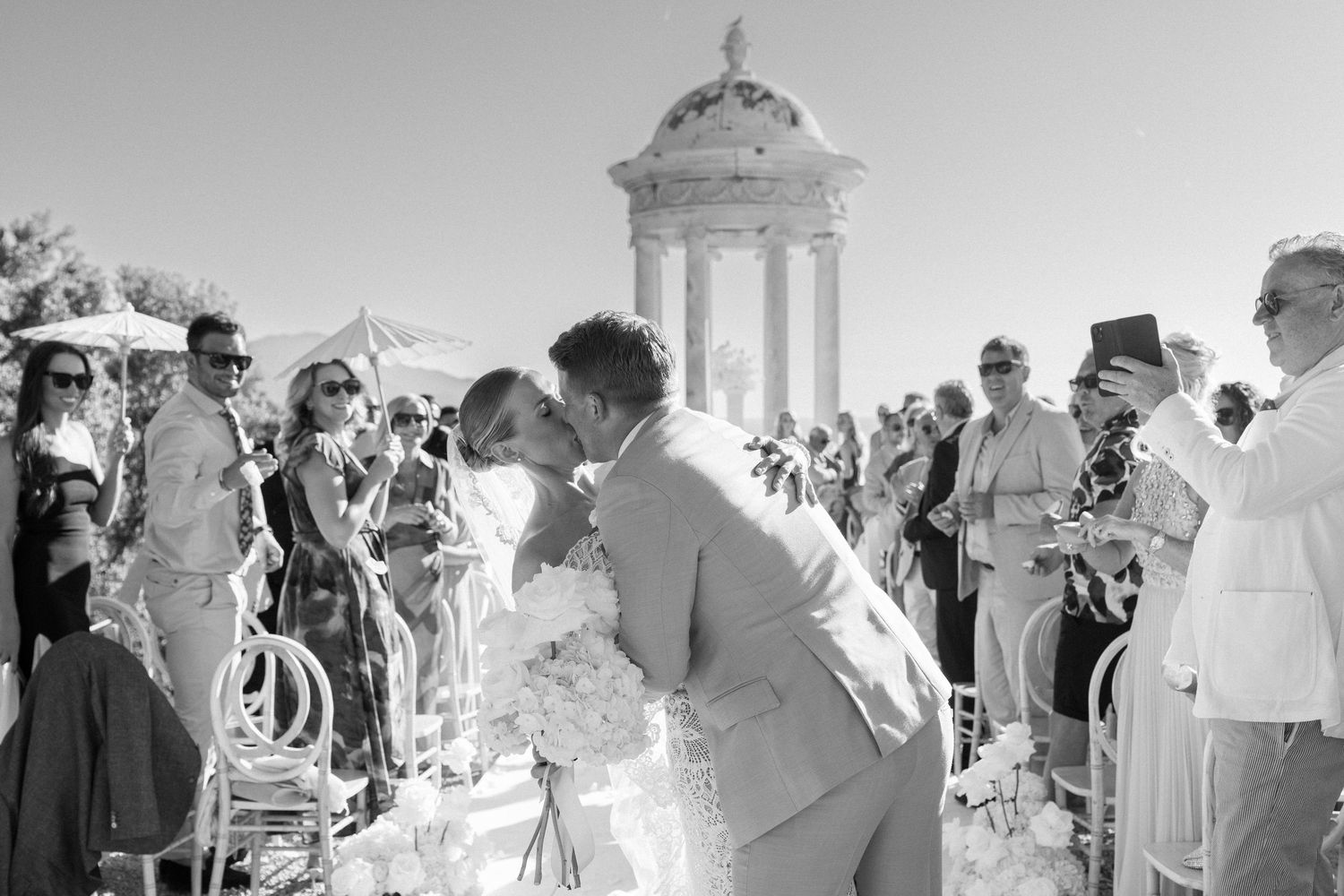 Guests mingle and celebrate at an elegant outdoor wedding reception under a sunny sky.