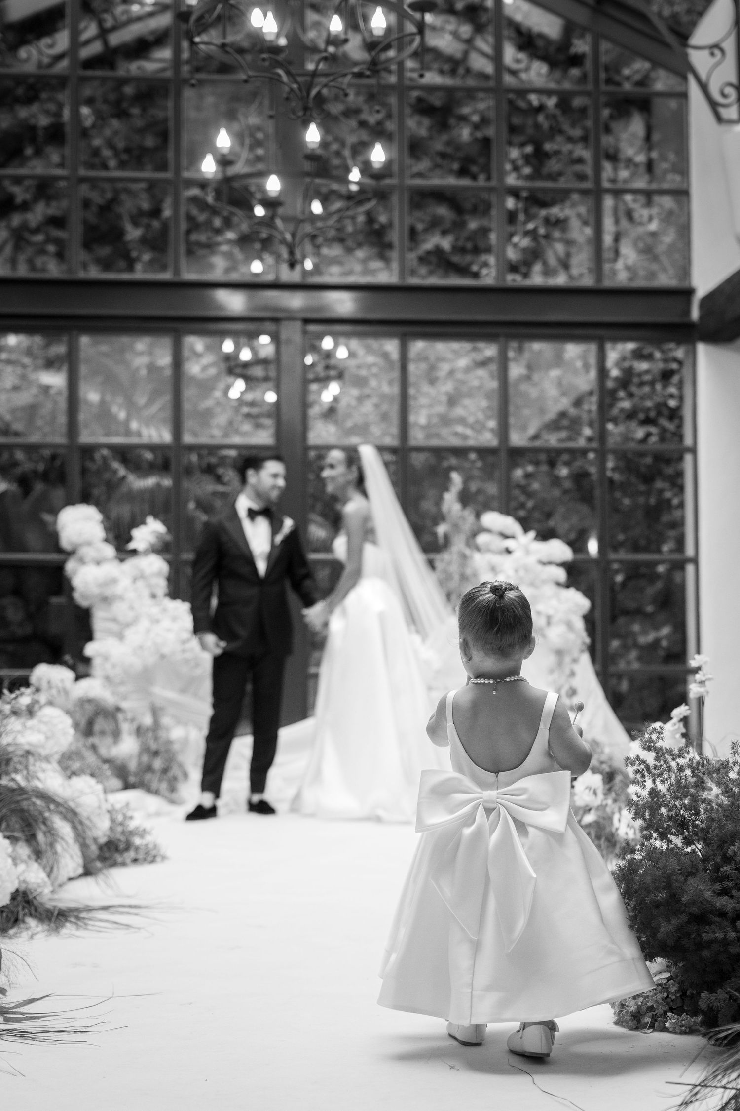 Black and white photo of wedding ceremony setup in glass conservatory with floral arrangements.