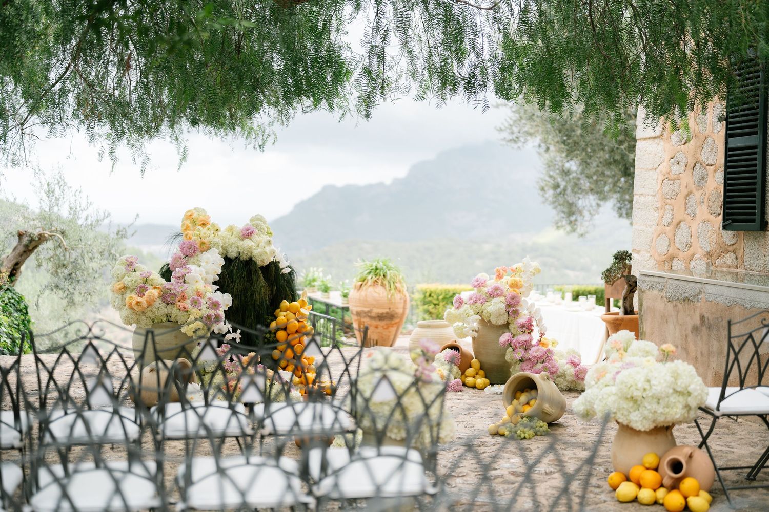 Floral arrangements and decorations on a terrace overlooking misty mountains with willow branches framing the view.
