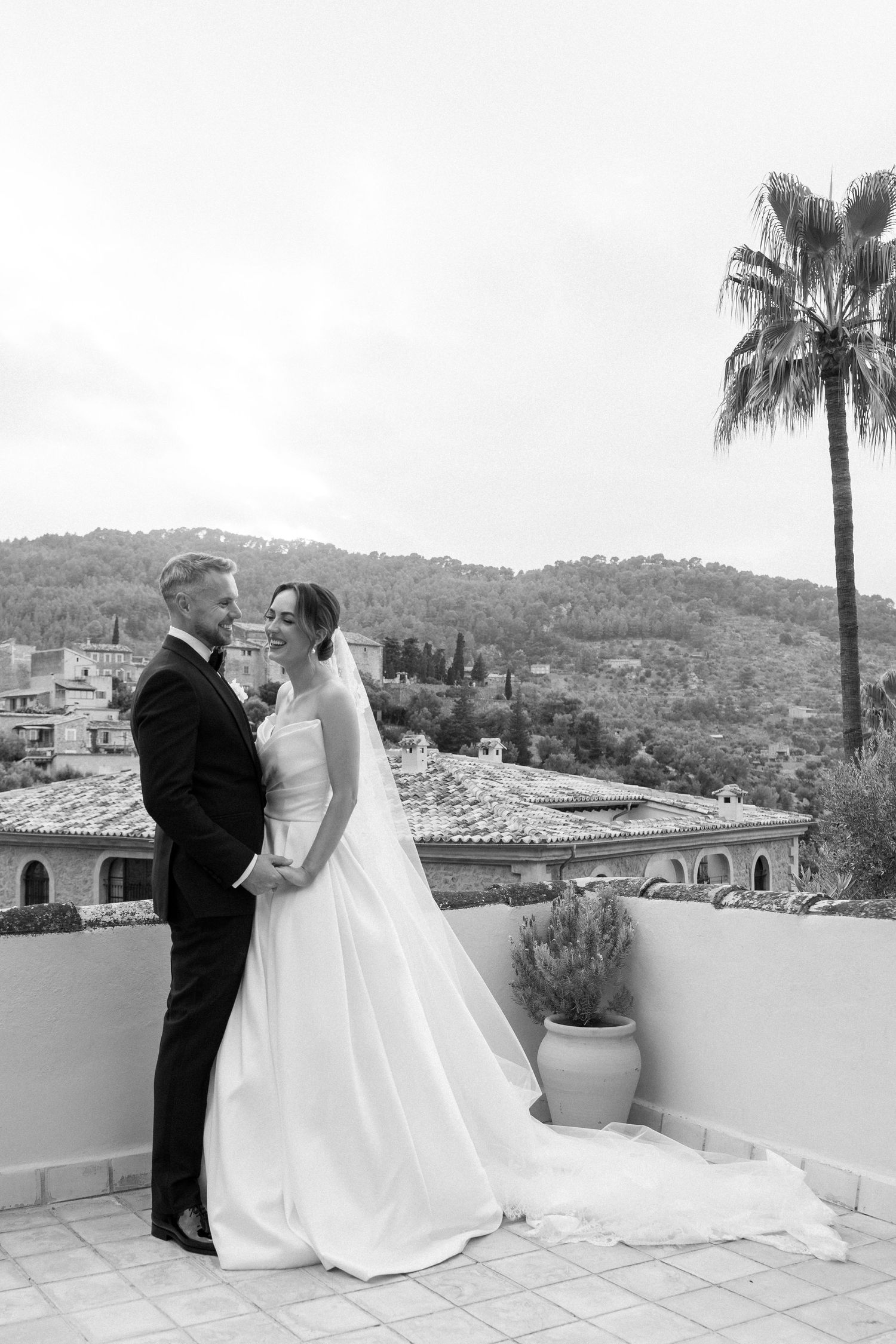 Wedding couple on a Mediterranean terrace with palm trees and mountain views.