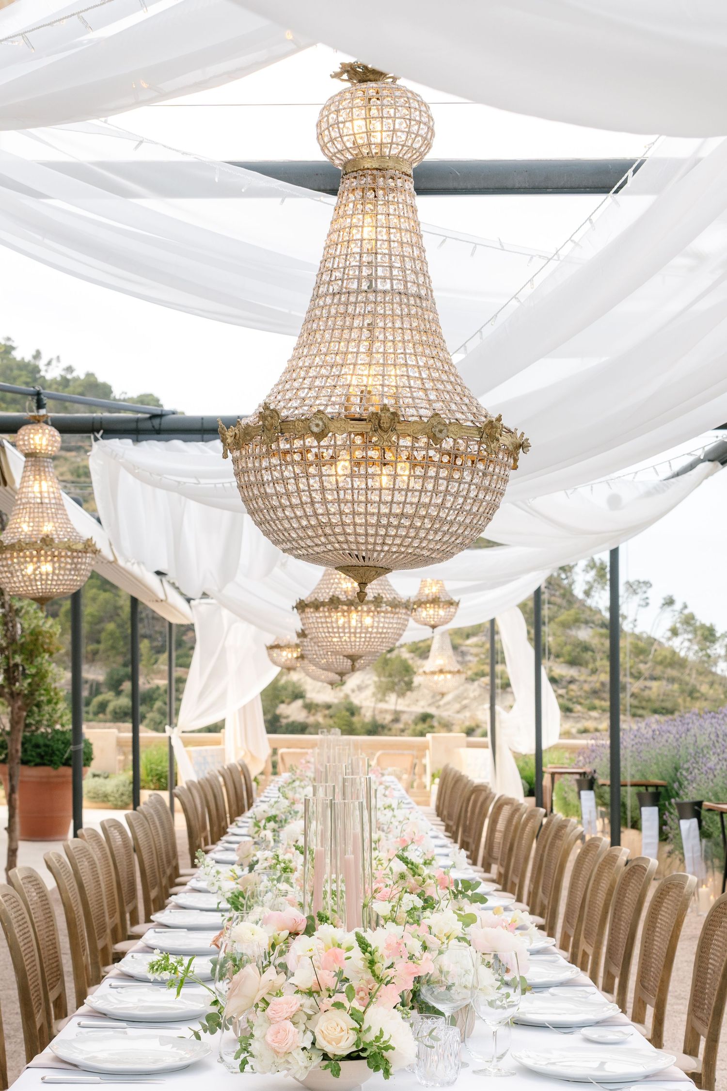 Elegant wedding reception setup with crystal chandeliers and white linens overlooking mountain views.