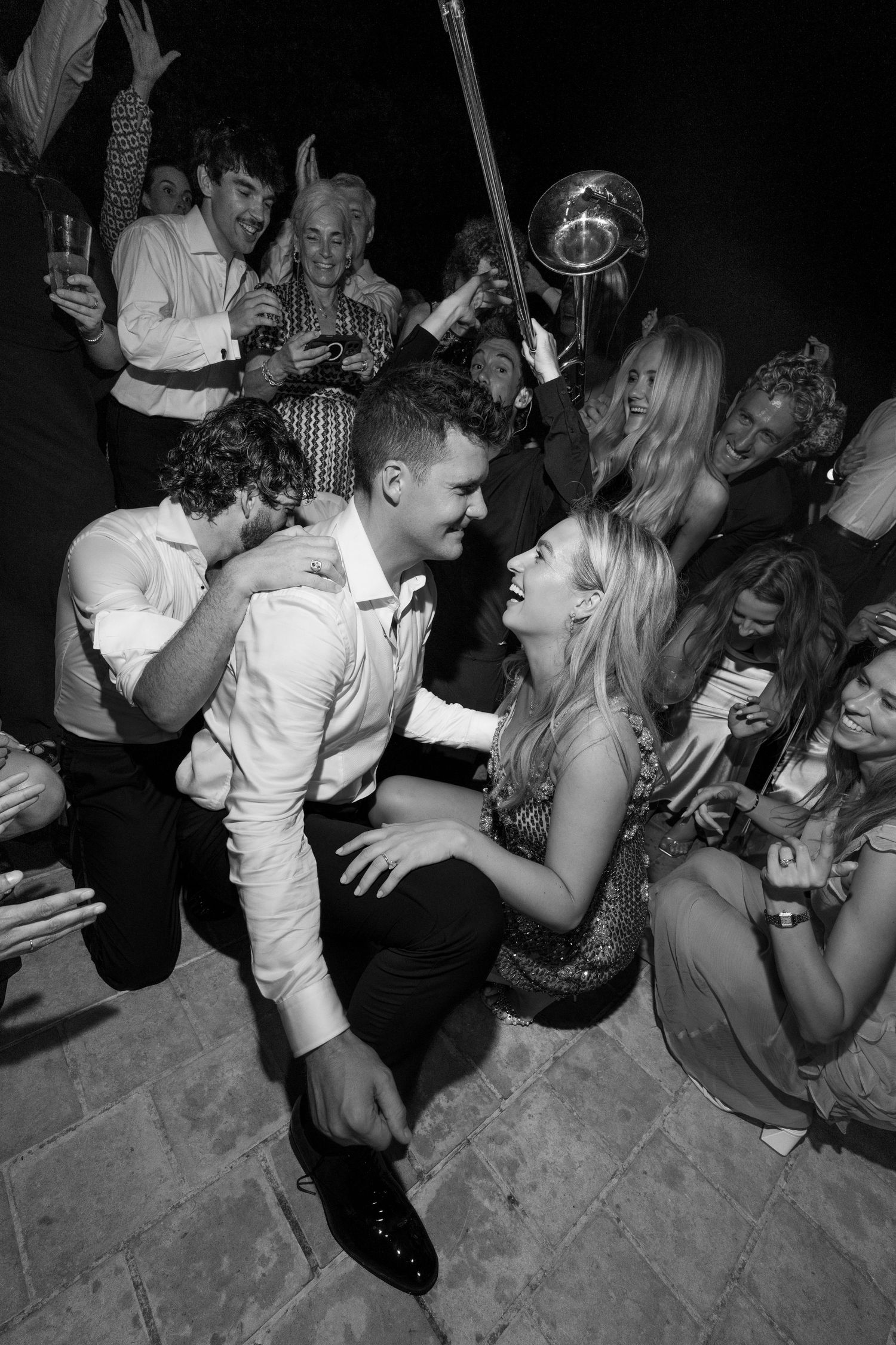 Black and white photo of a joyful couple dancing on the floor surrounded by celebrating guests at a lively party.