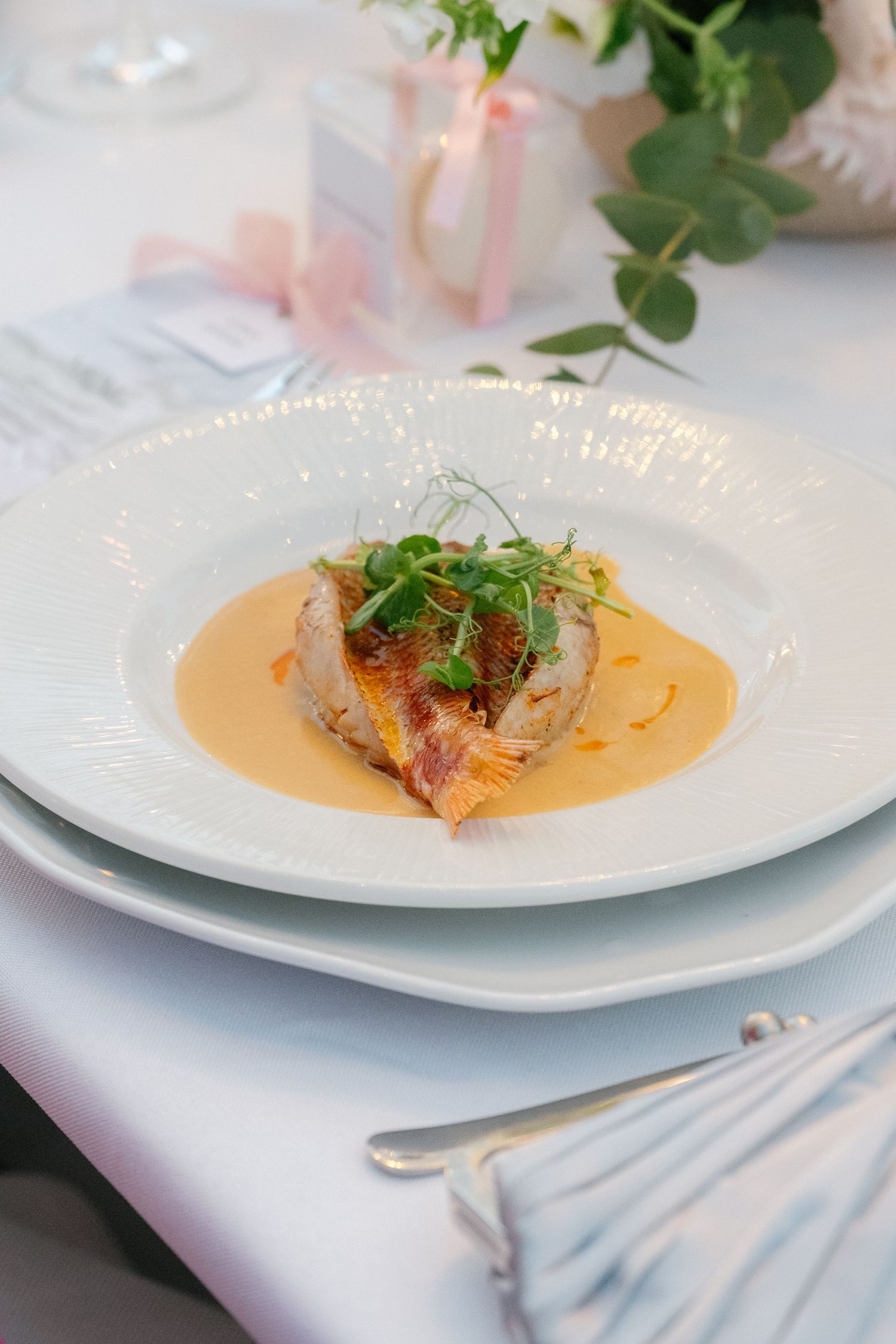 Elegant plated seafood dish with orange sauce and garnish served on white china at upscale restaurant.