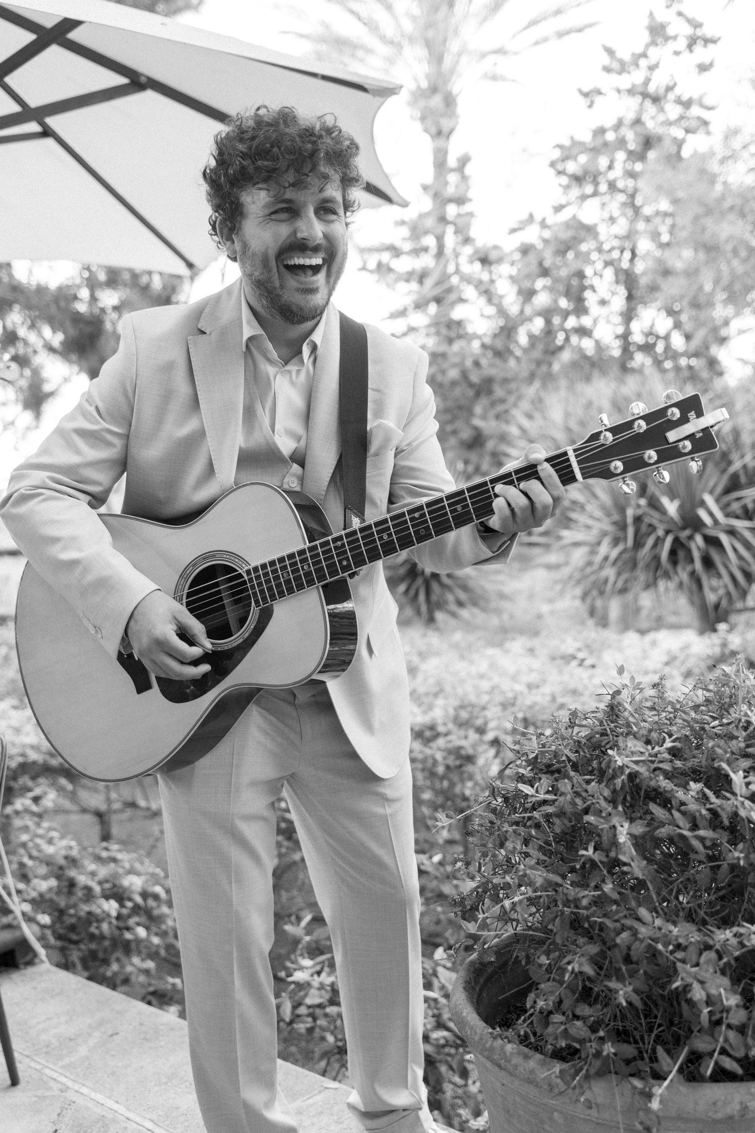 Musicians in light suits play acoustic guitars outdoors at an elegant event.