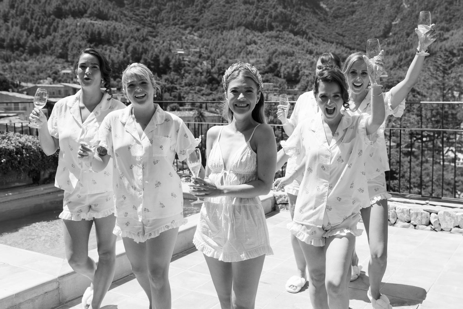 Wedding party celebrates outdoors in bright sunlight wearing white attire.