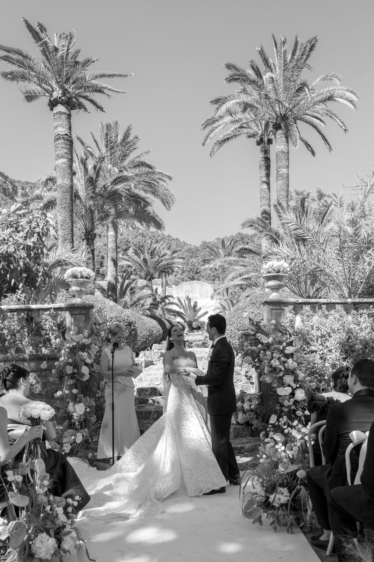 Bride and groom exchange vows at outdoor wedding ceremony surrounded by lush palm trees and floral arrangements.