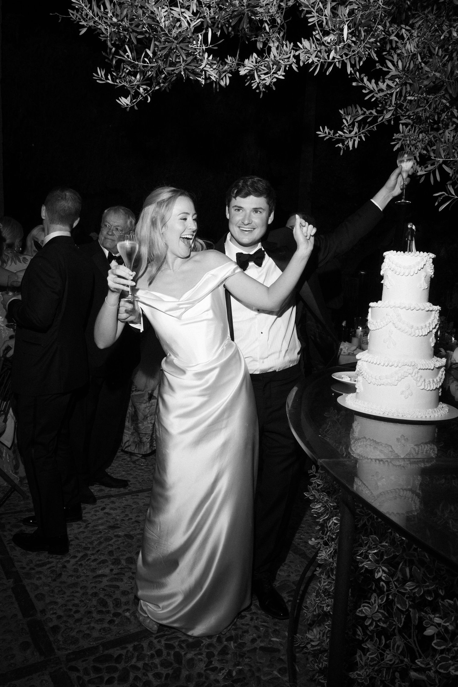 Wedding reception at night featuring white wedding cake and dancing under olive trees.