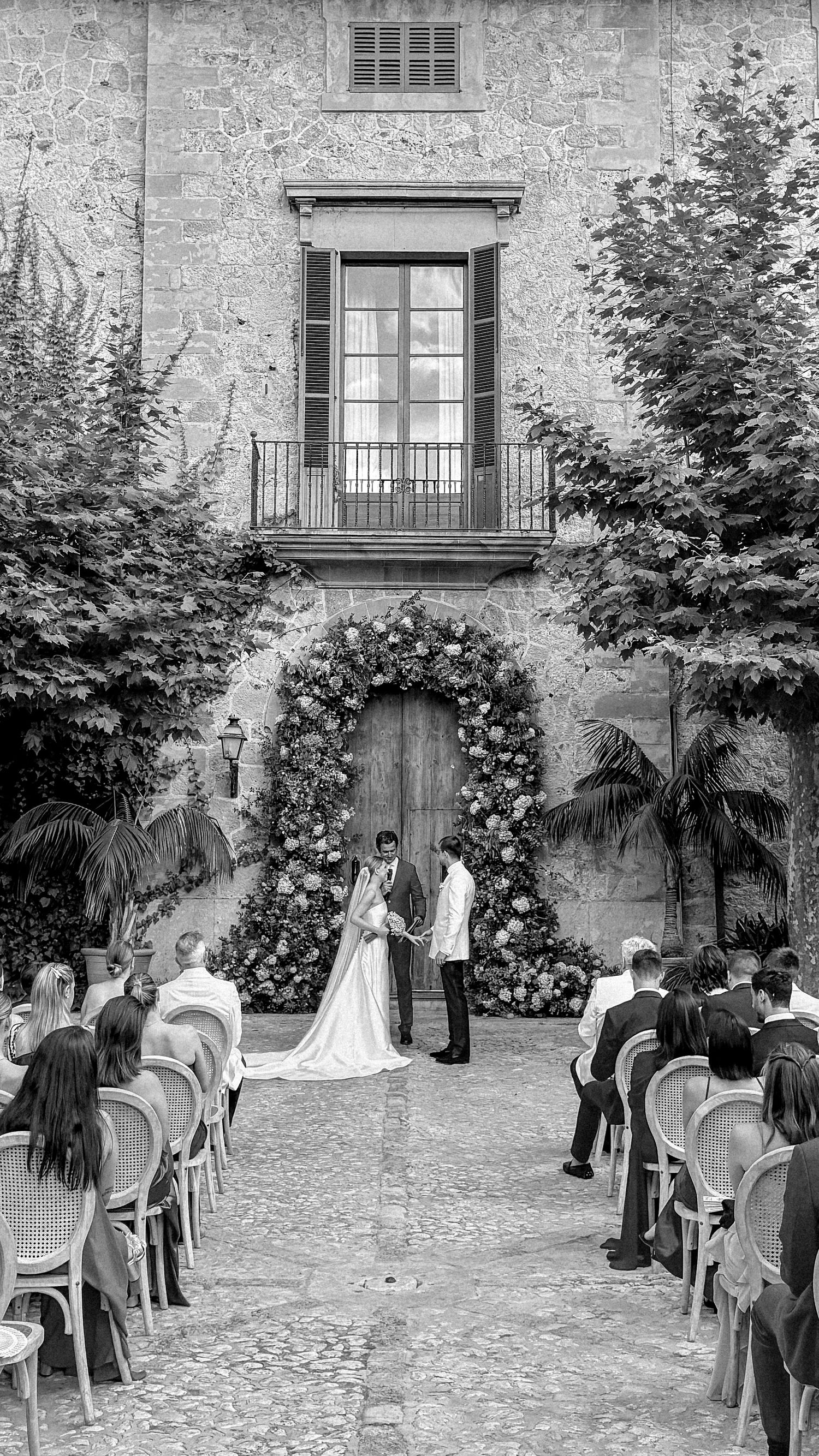 Wedding ceremony in progress at a historic stone courtyard with natural landscaping.