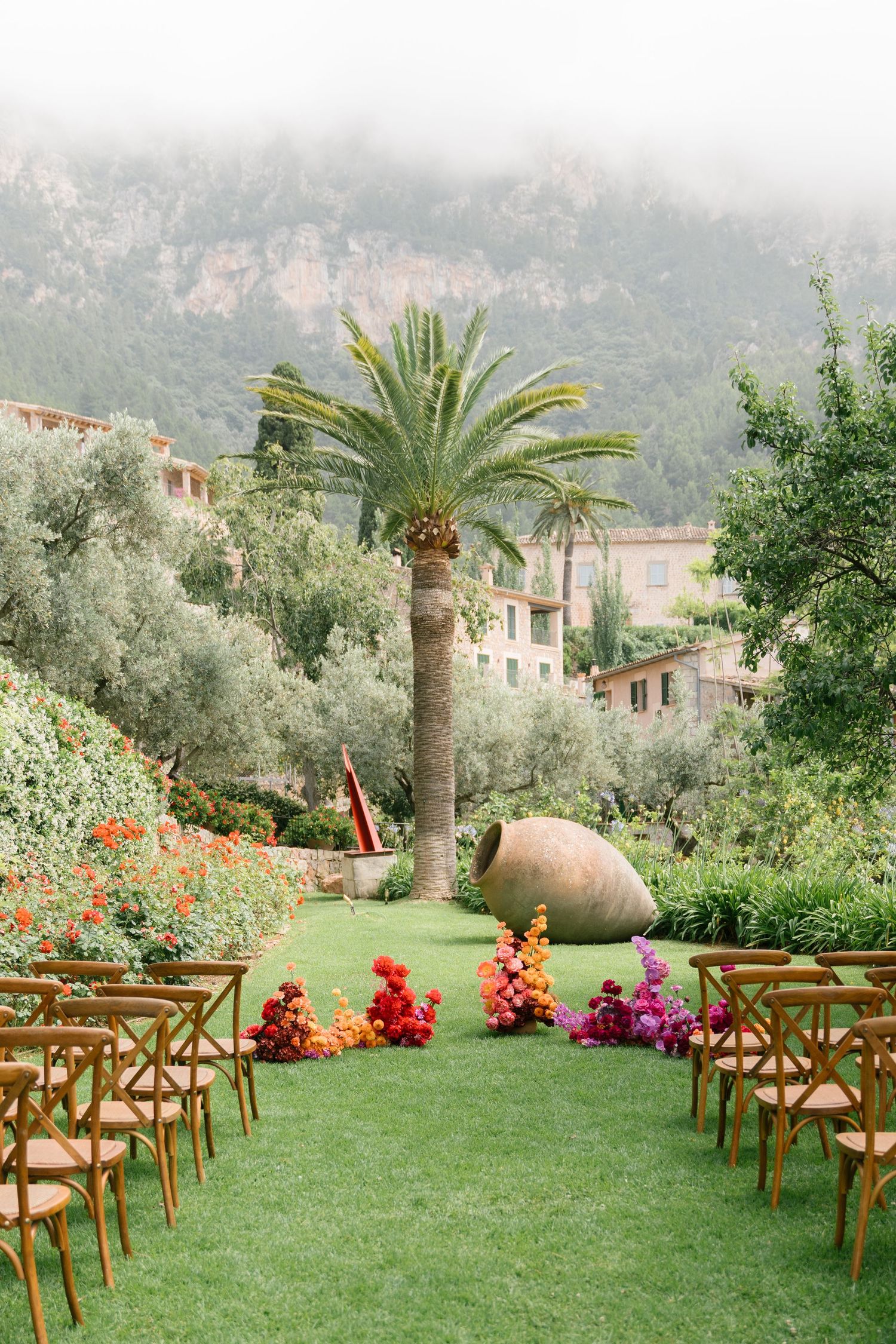 Outdoor wedding ceremony setup with wooden chairs and colorful floral arrangements.