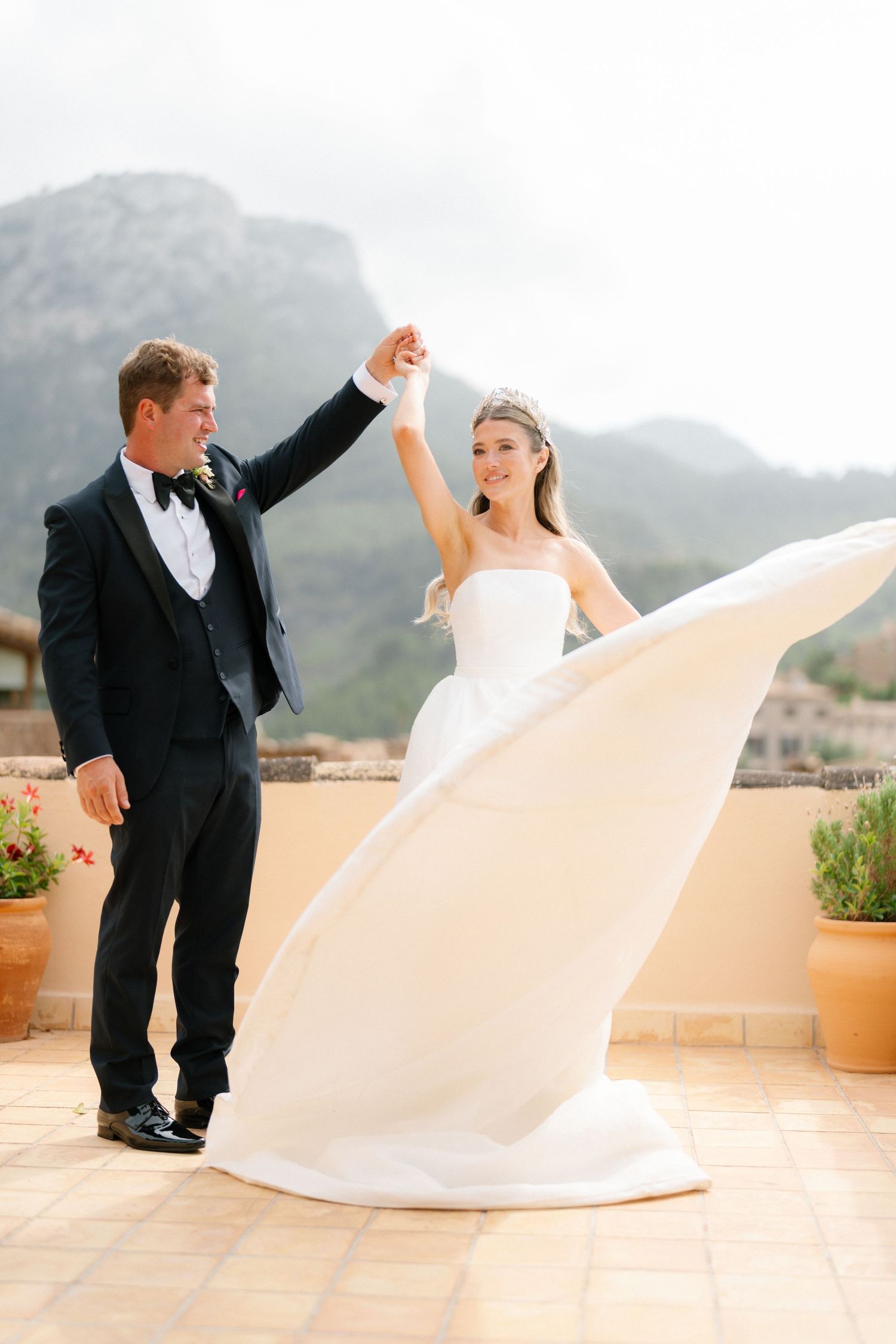 Wedding couple dances on terrace with flowing white dress against mountain backdrop.