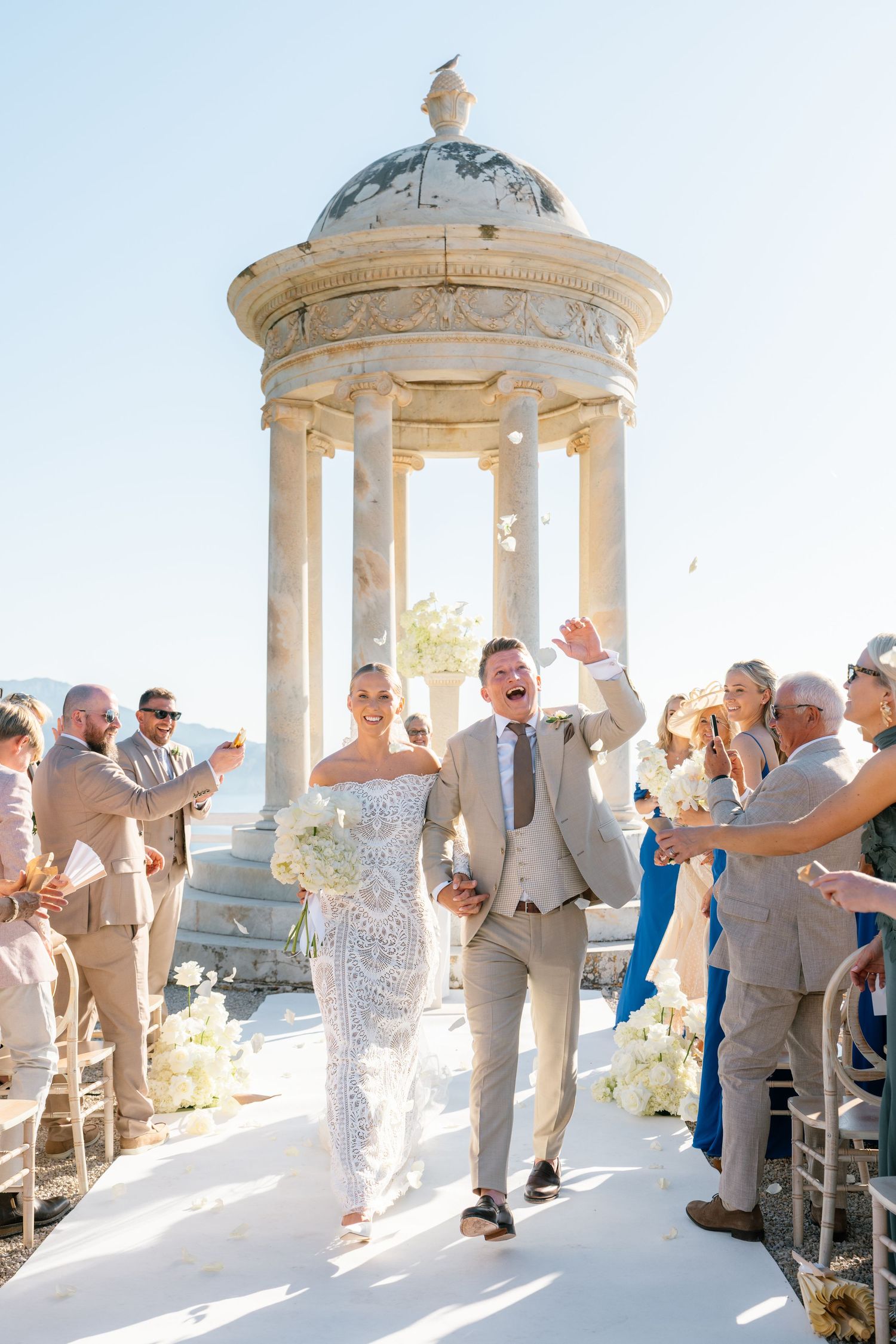 Wedding celebration at a Mediterranean gazebo with guests in formal attire.